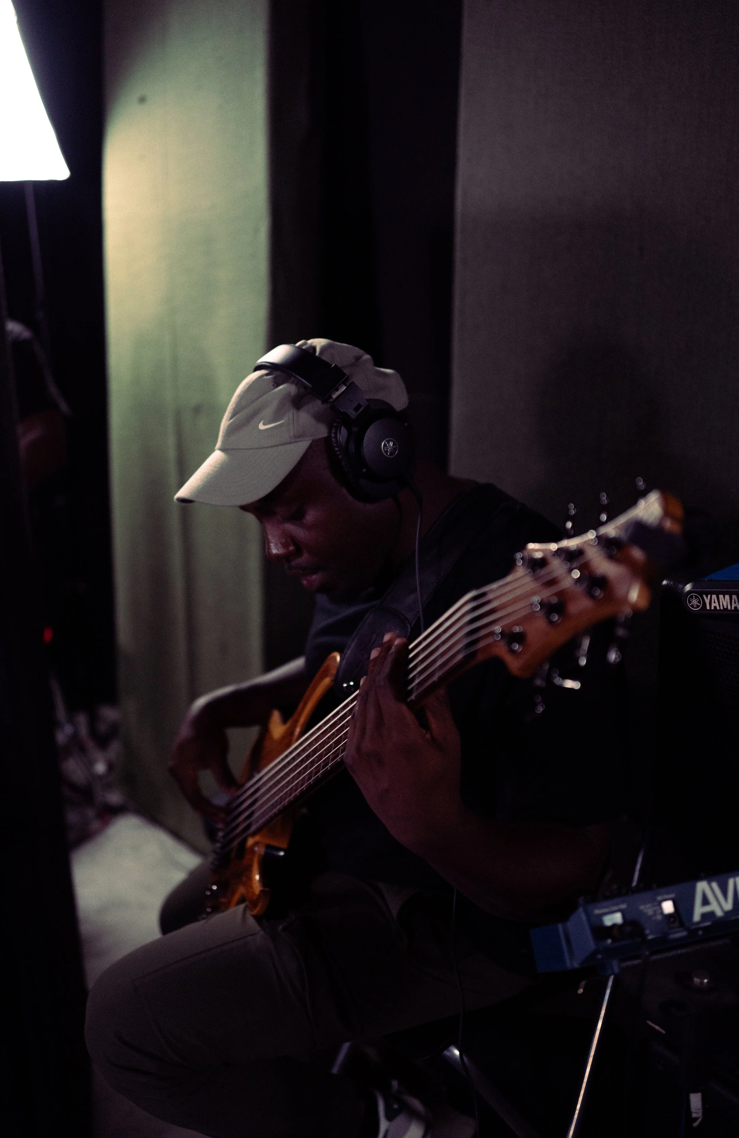 A person wearing a beige Nike cap and large headphones playing an acoustic guitar in a recording or practice space.