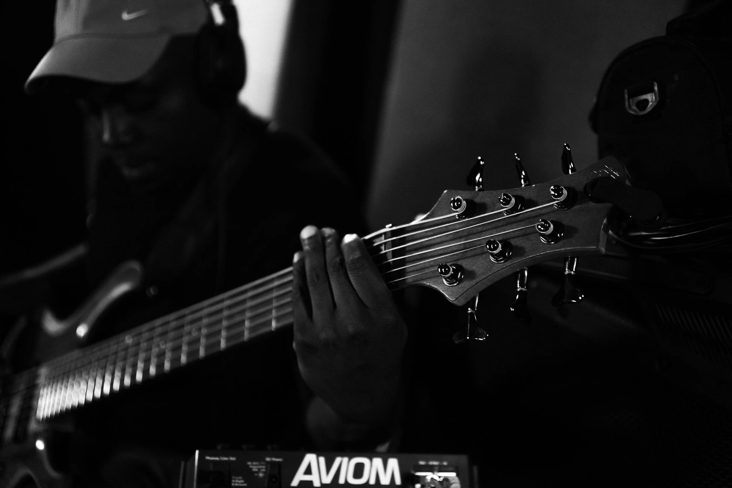 A person wearing a cap and glasses playing an acoustic guitar in a dimly lit room.