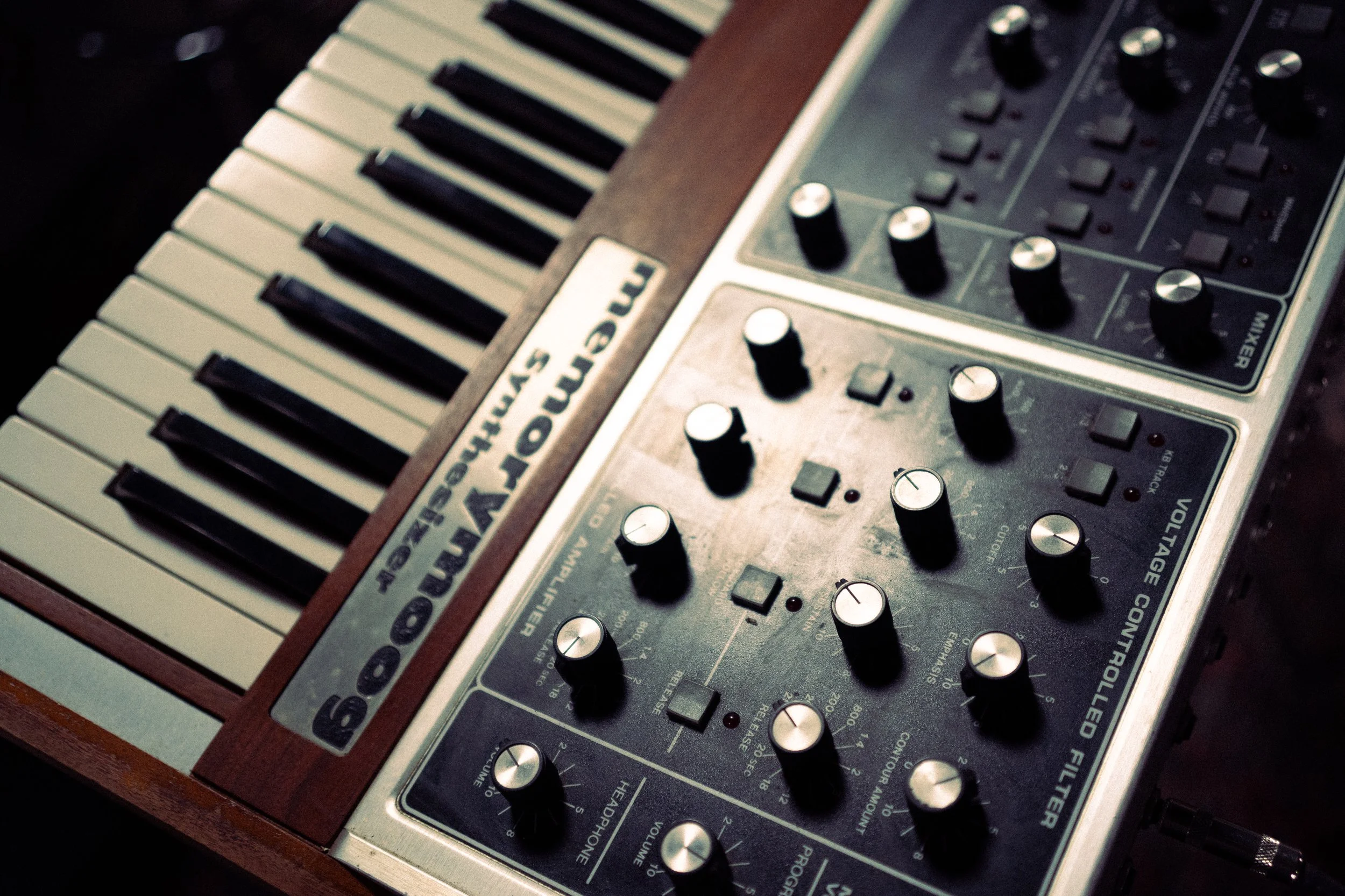 A vintage Moog synthesizer with black and white keyboard, multiple control knobs, switches, and sliders.