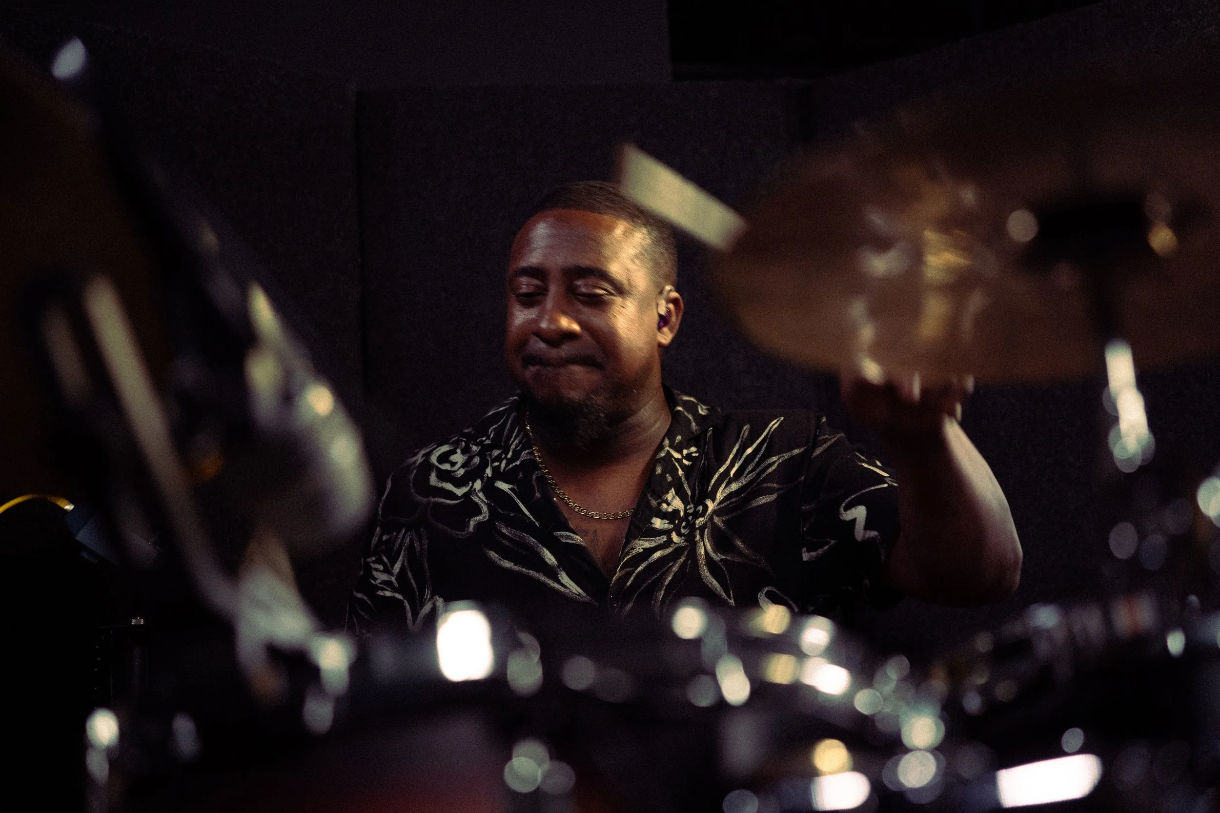 A male drummer playing drums with a focused expression in a dark setting.
