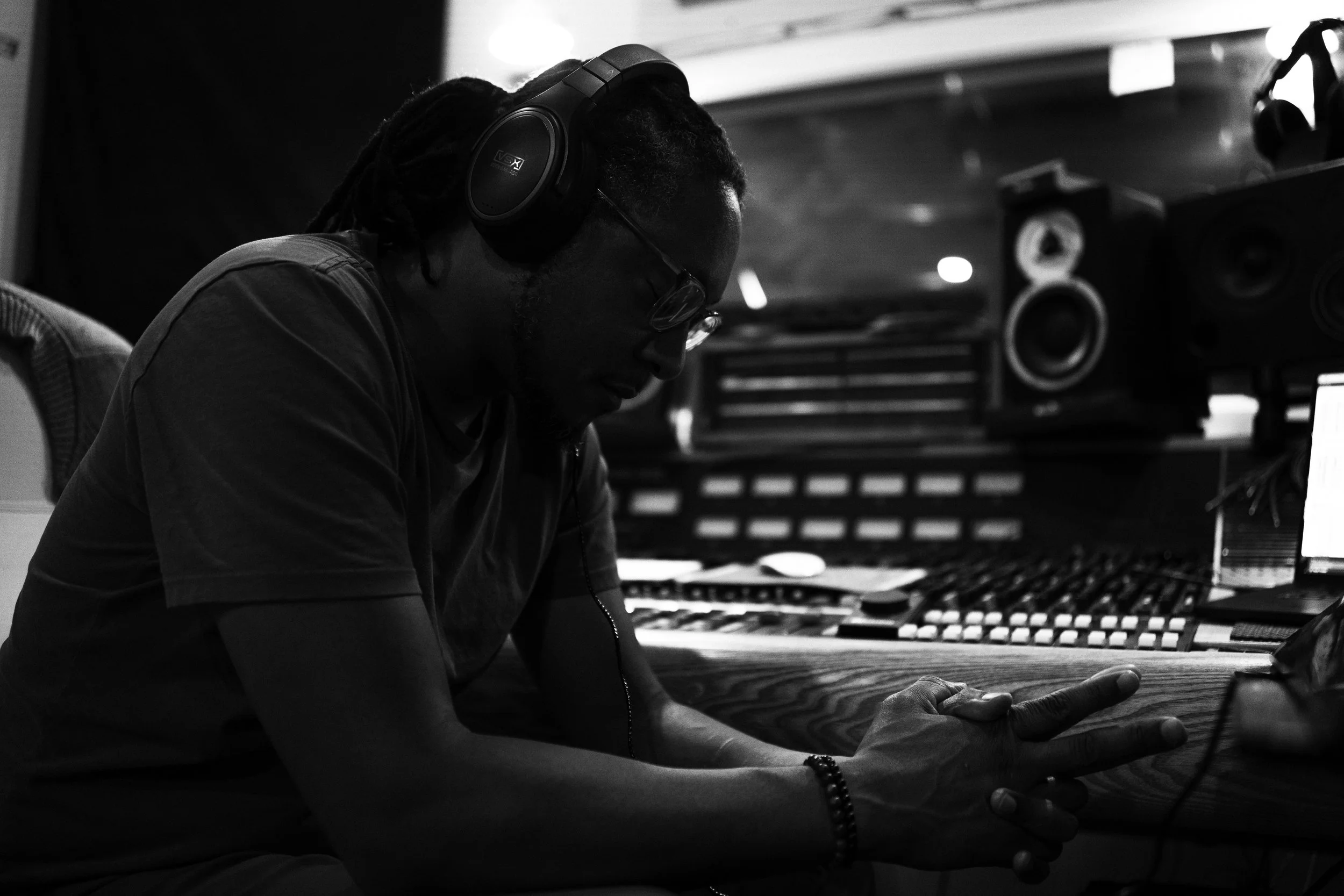 A man wearing headphones and glasses in a recording studio working at a sound mixing console.