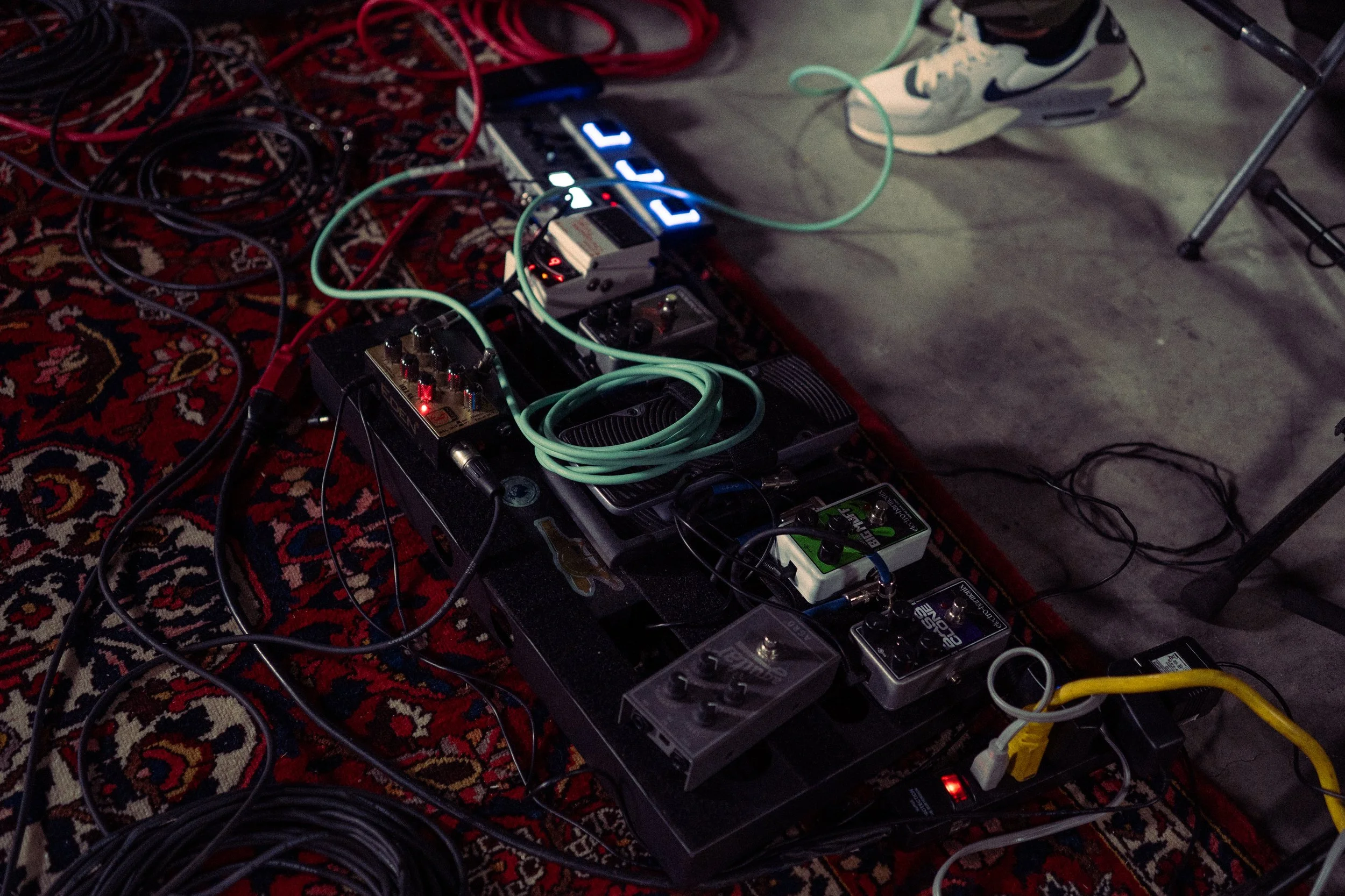 A collection of guitar effects pedals, cables, and a digital pedal on a patterned rug in a music setup.