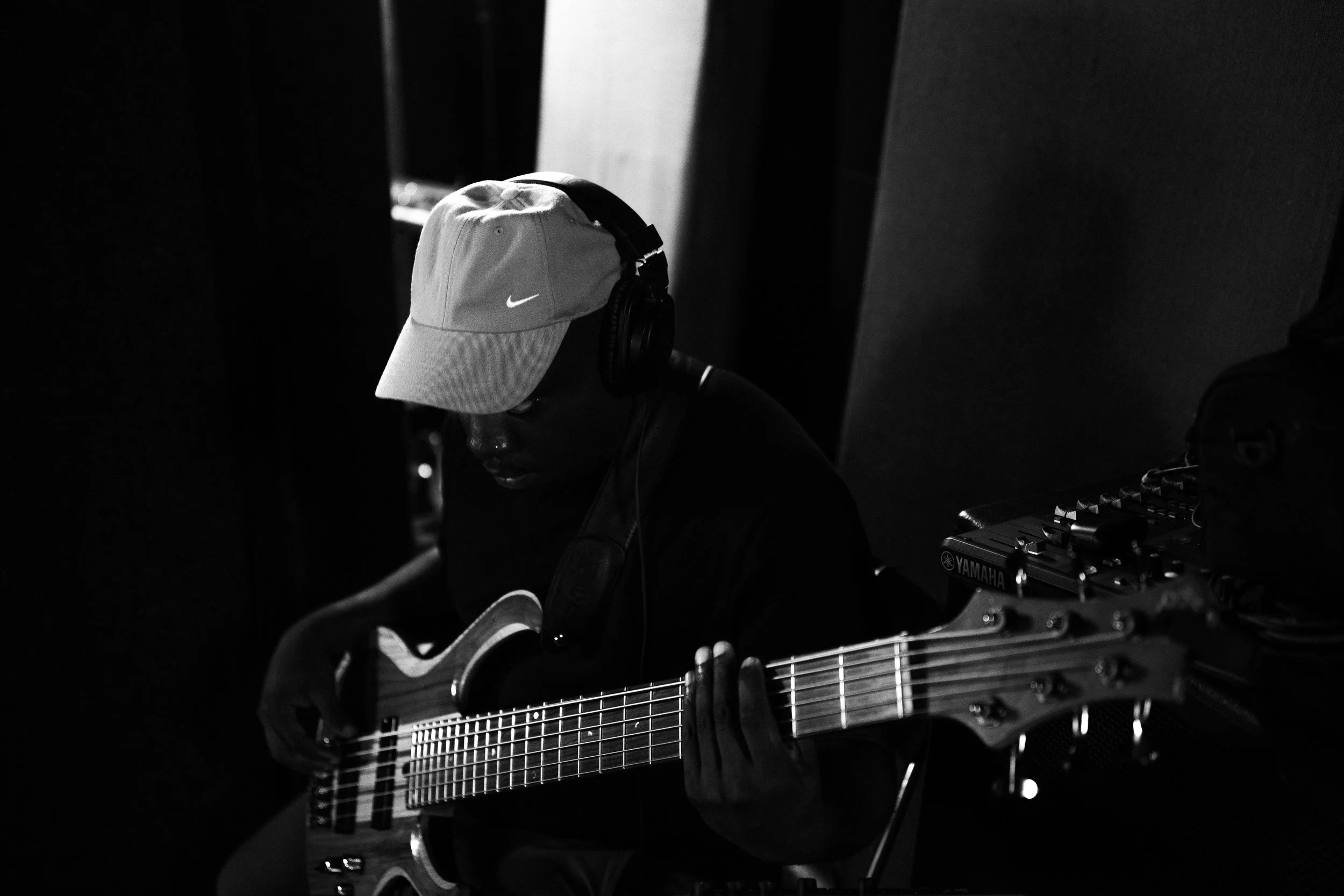 Person wearing a Nike cap and headphones playing an electric guitar in a dimly lit room.