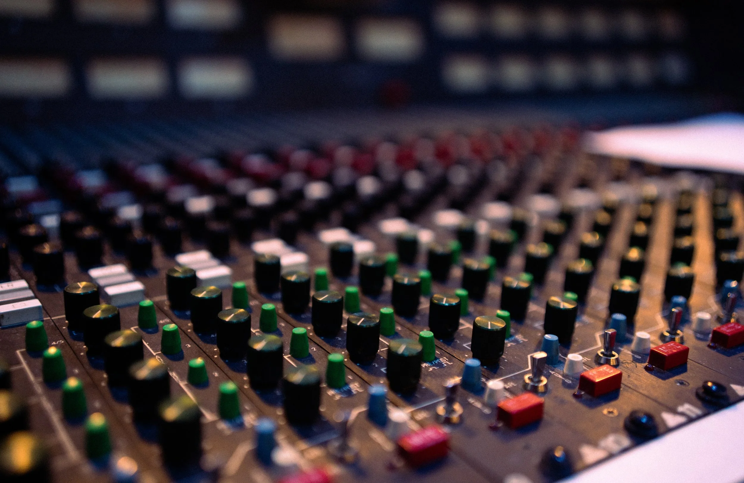 Close-up of a professional music mixing console with multiple colorful knobs and sliders, used in audio production.