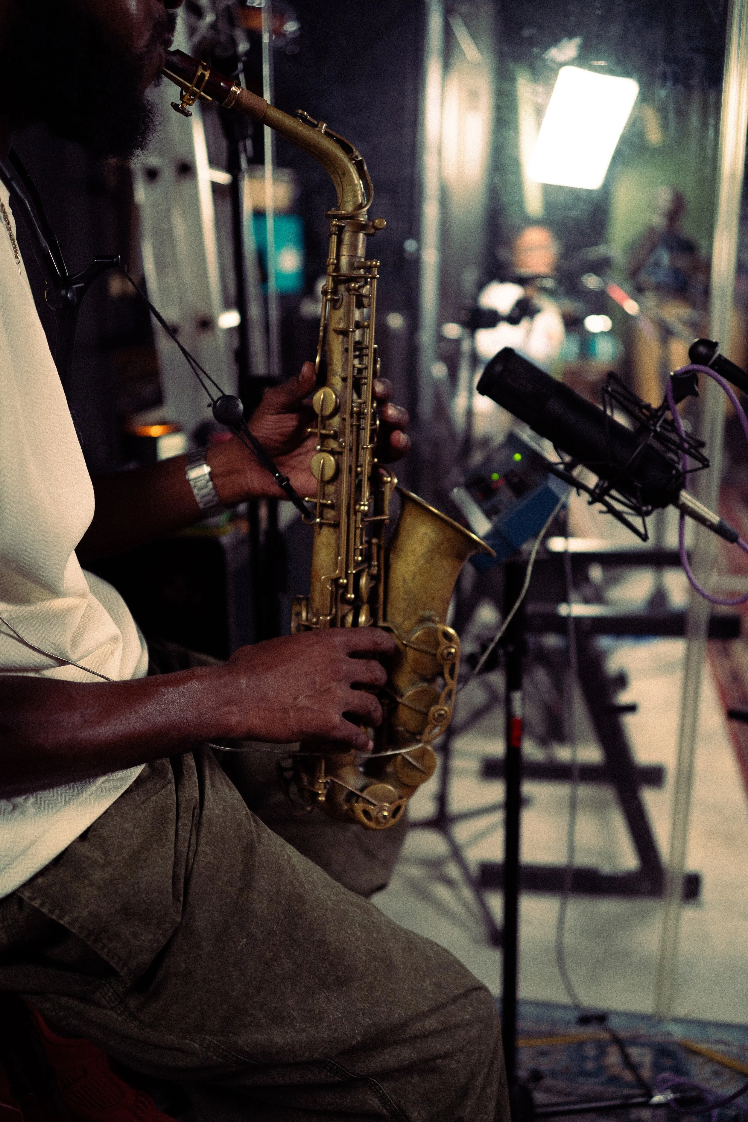 A person playing a saxophone in a recording studio with a microphone and soundproof glass behind him.
