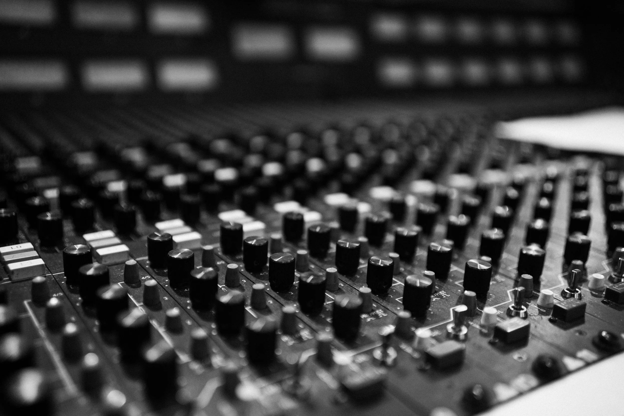 Close-up of a professional audio mixing console with numerous knobs and sliders, in black and white.