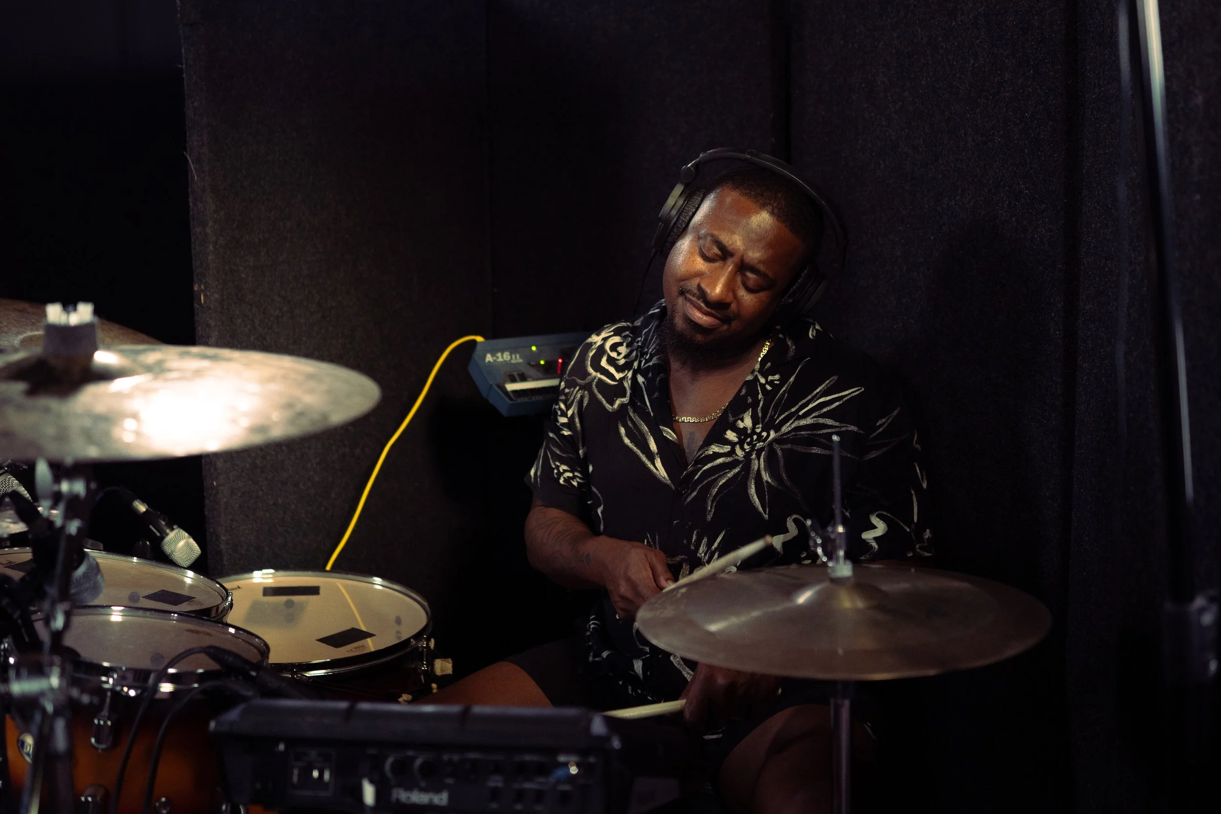 A man with headphones playing drums in a recording studio.
