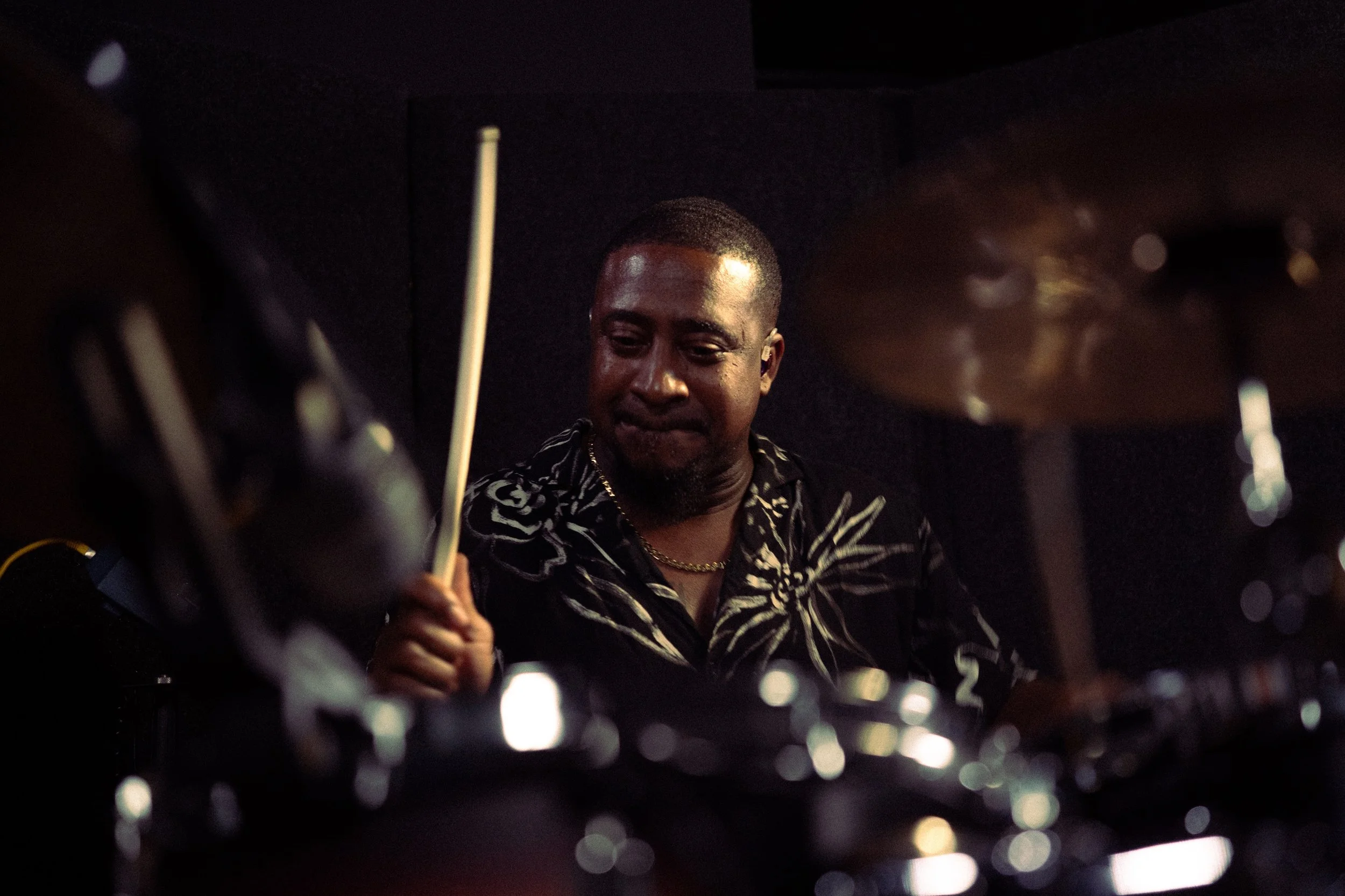 A man playing the drums in a dimly lit room, focused on his performance.