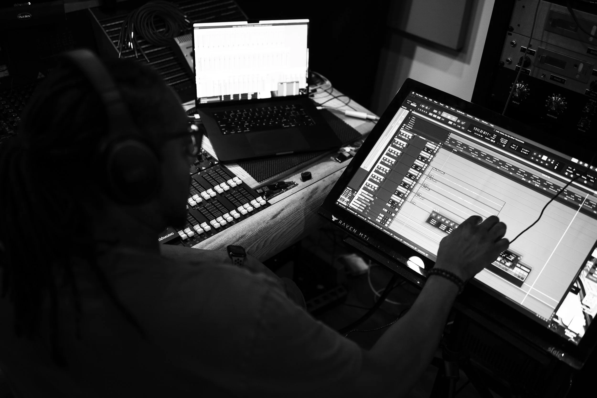 Person wearing headphones working on audio production on large computer screen with digital audio workstation layout.
