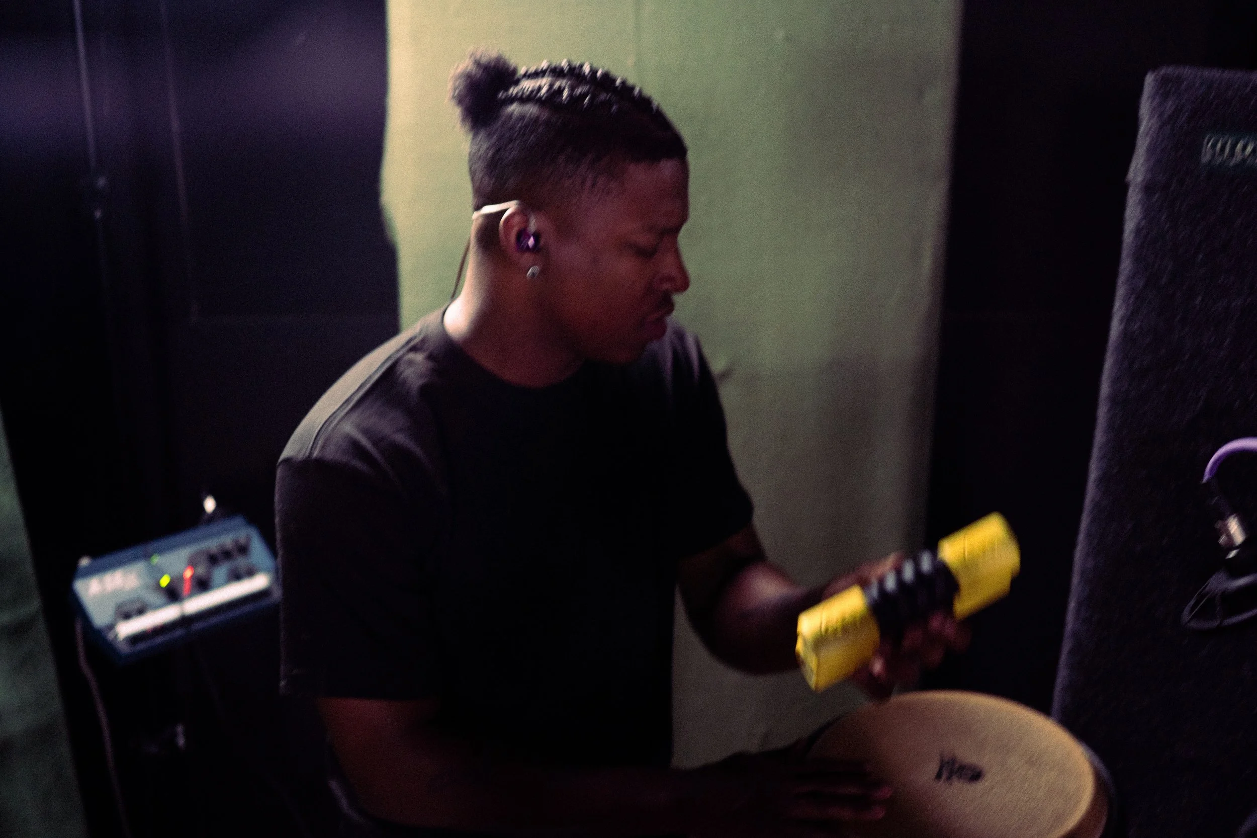 Person playing the drums, wearing headphones, in a dark room with musical equipment.