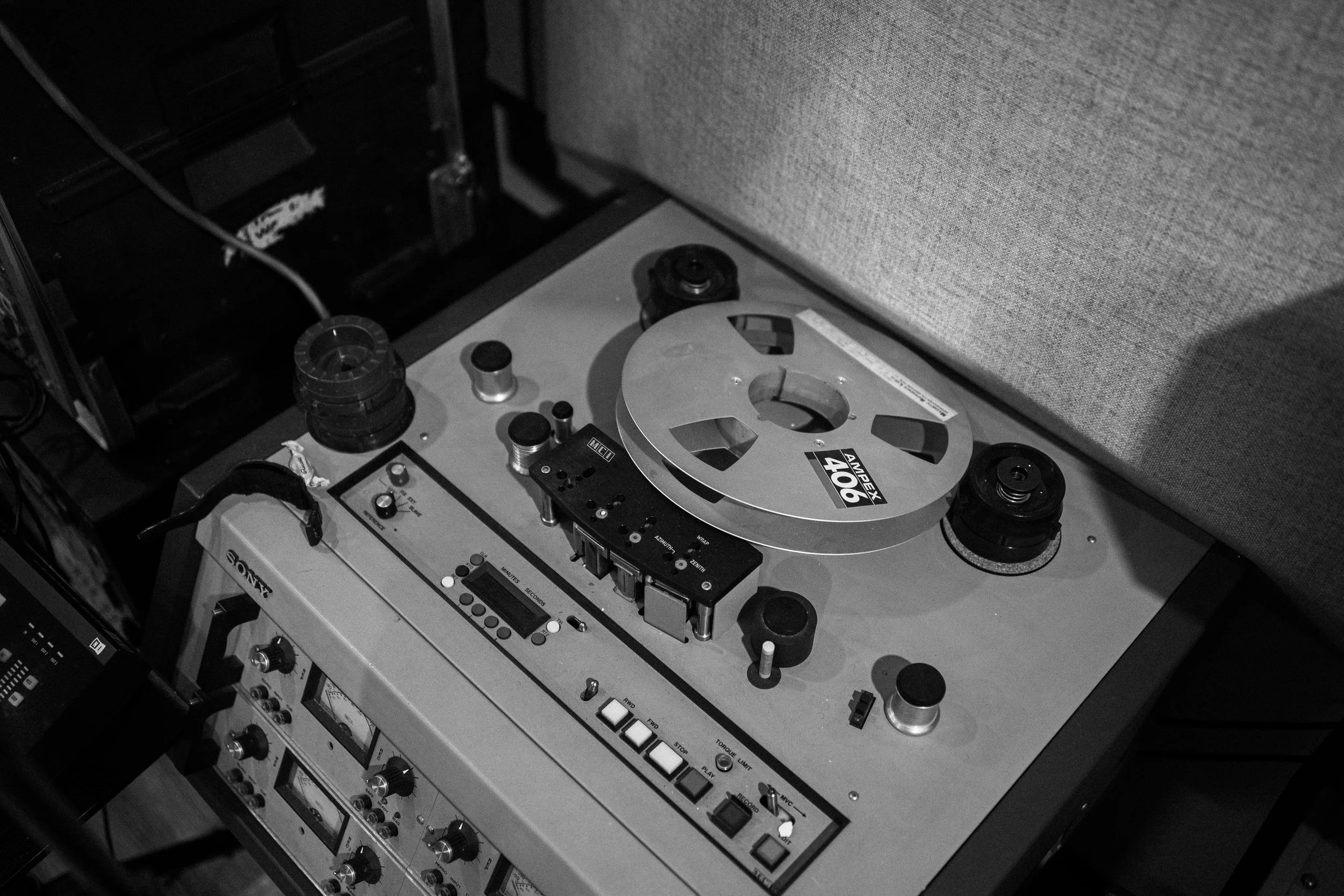 A vintage reel-to-reel tape recorder with several knobs and buttons, placed on a table next to a sofa.