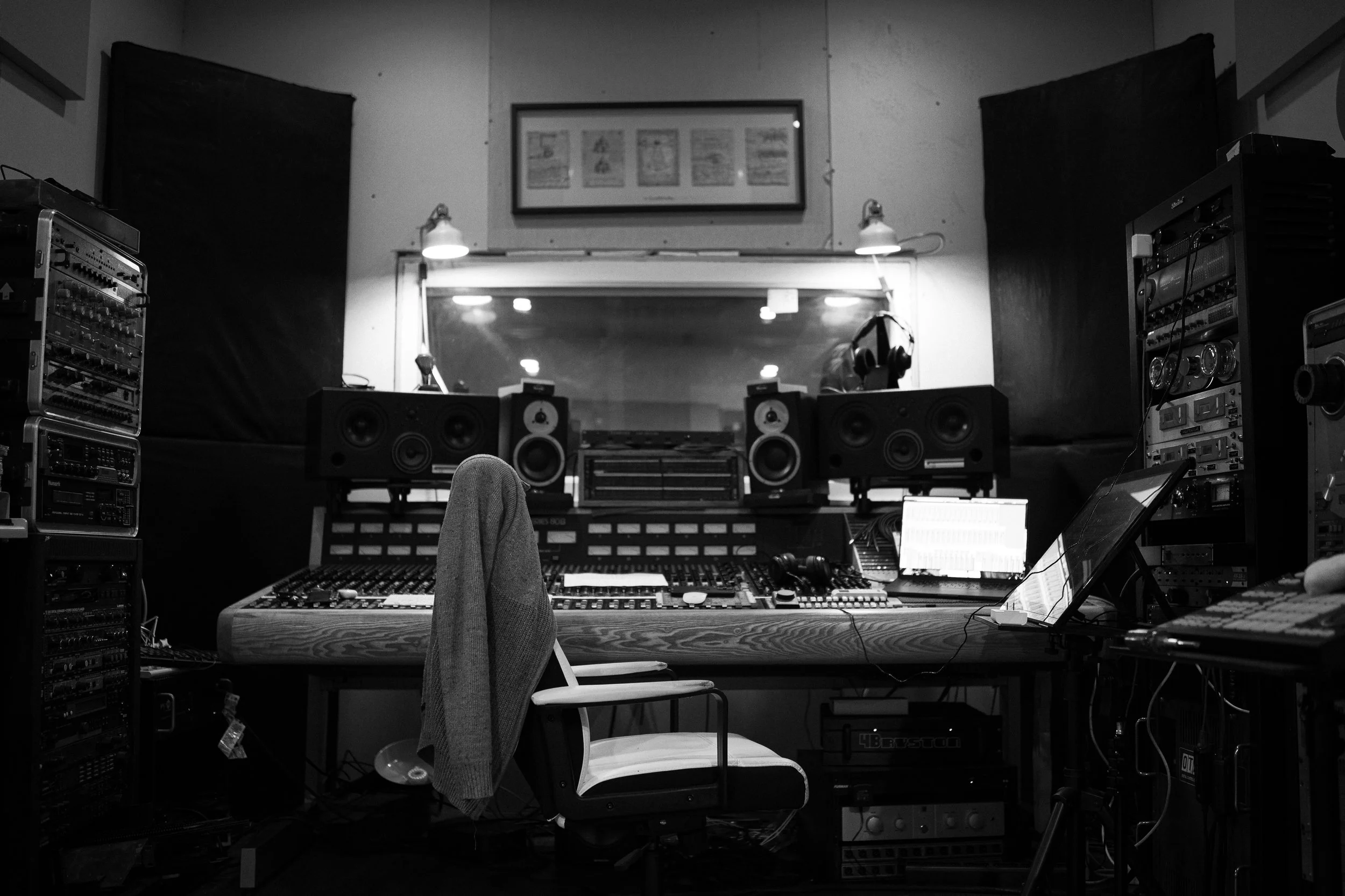 Black and white photo of a recording studio control room with a mixing console, speakers, headphones, and various electronic equipment.