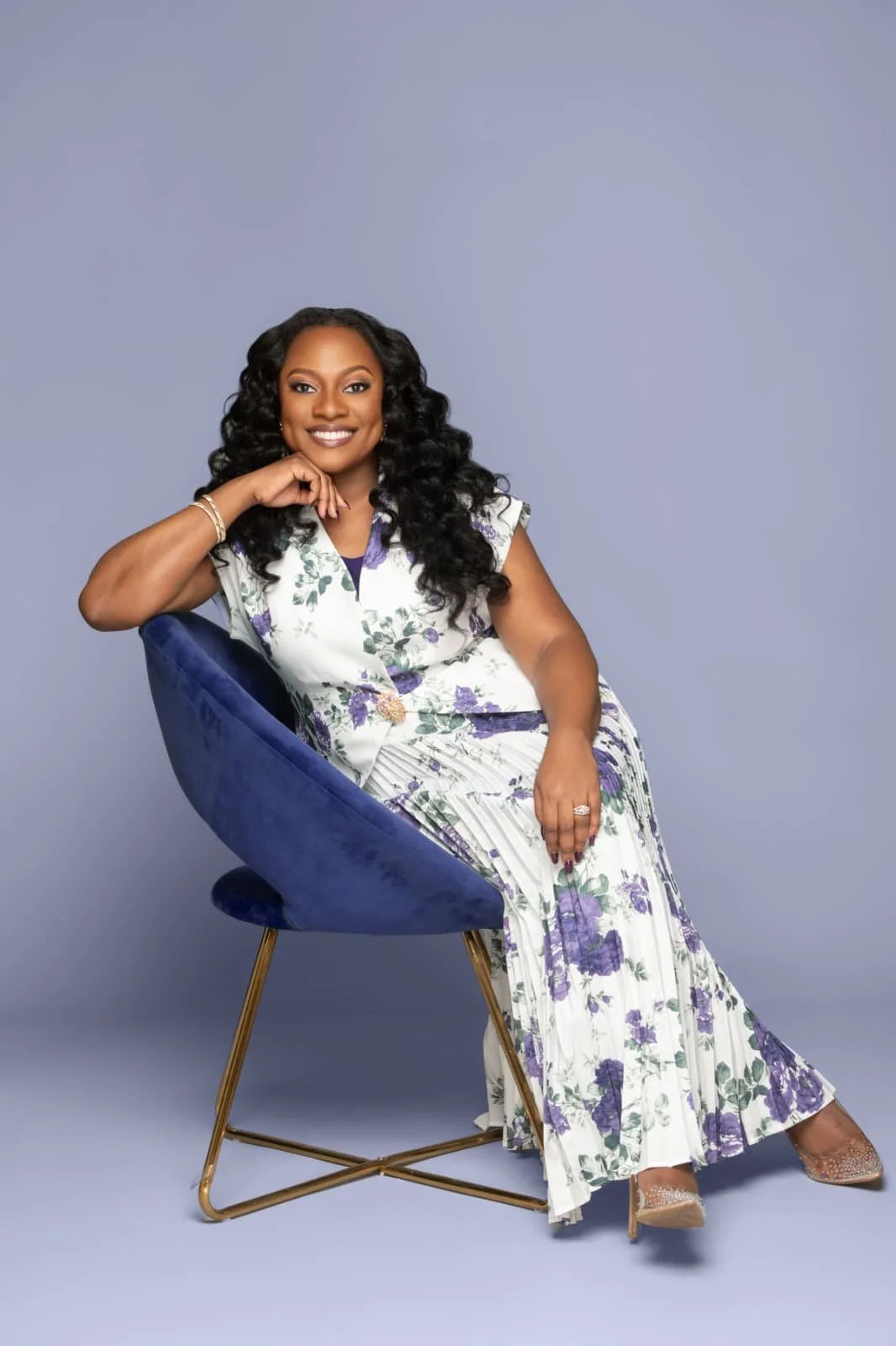 Dr. Uzoma in purple and white floral skirt set, sitting in a purple chair