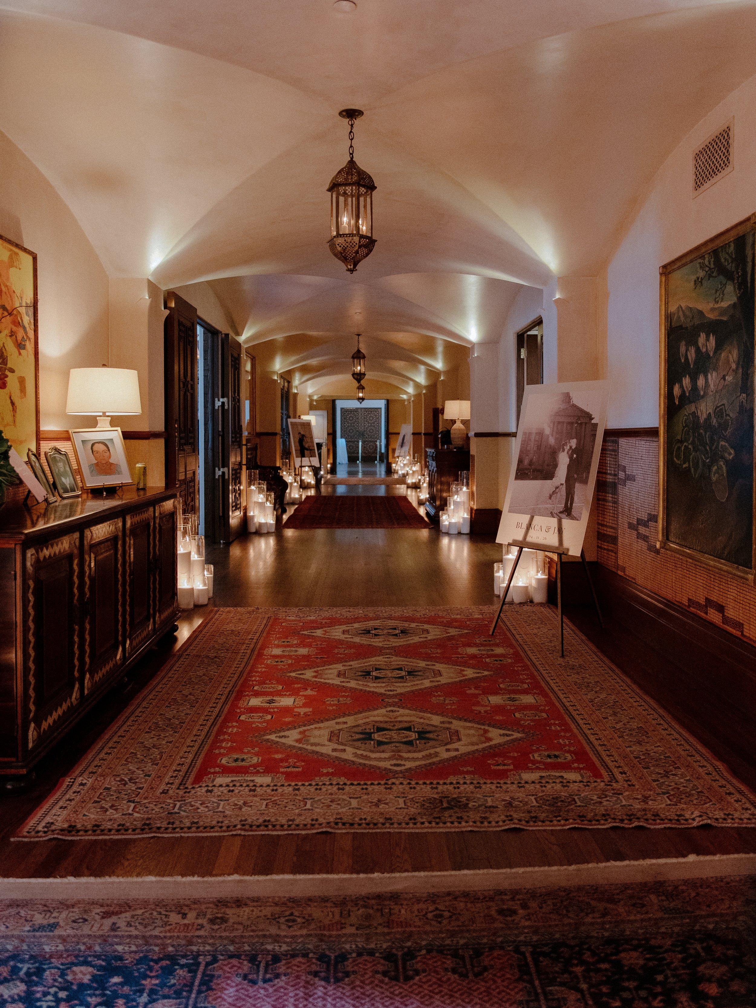 Candlelit barrel-vaulted hallway with an antique lantern, layered rugs and framed portraits