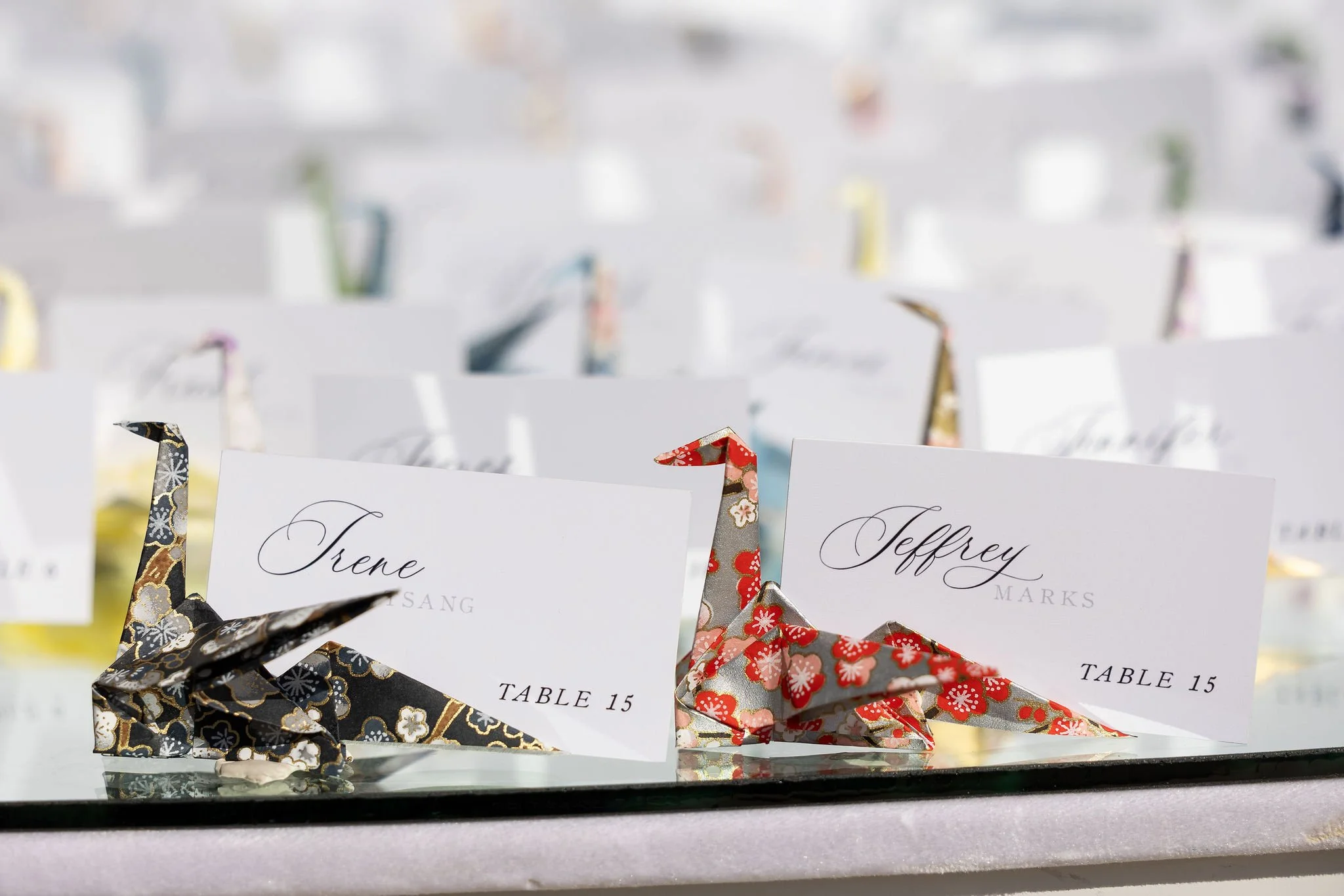 colorful origami birds escort cards on a glass table for guest seating assignments for Asian Wedding