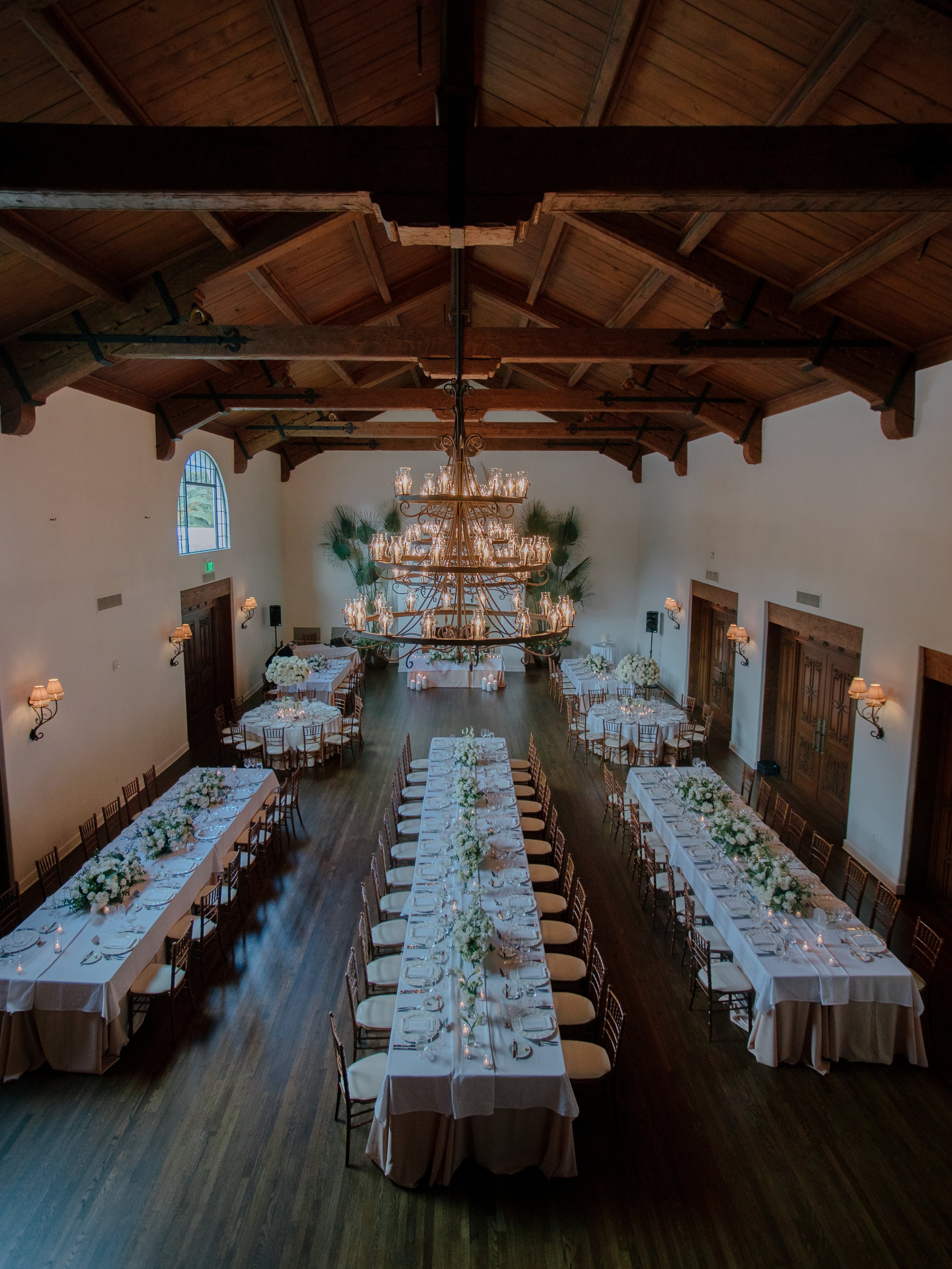 Long banquet tables set beneath the Great Room's wood-beamed ceiling and wrought iron chandeliers