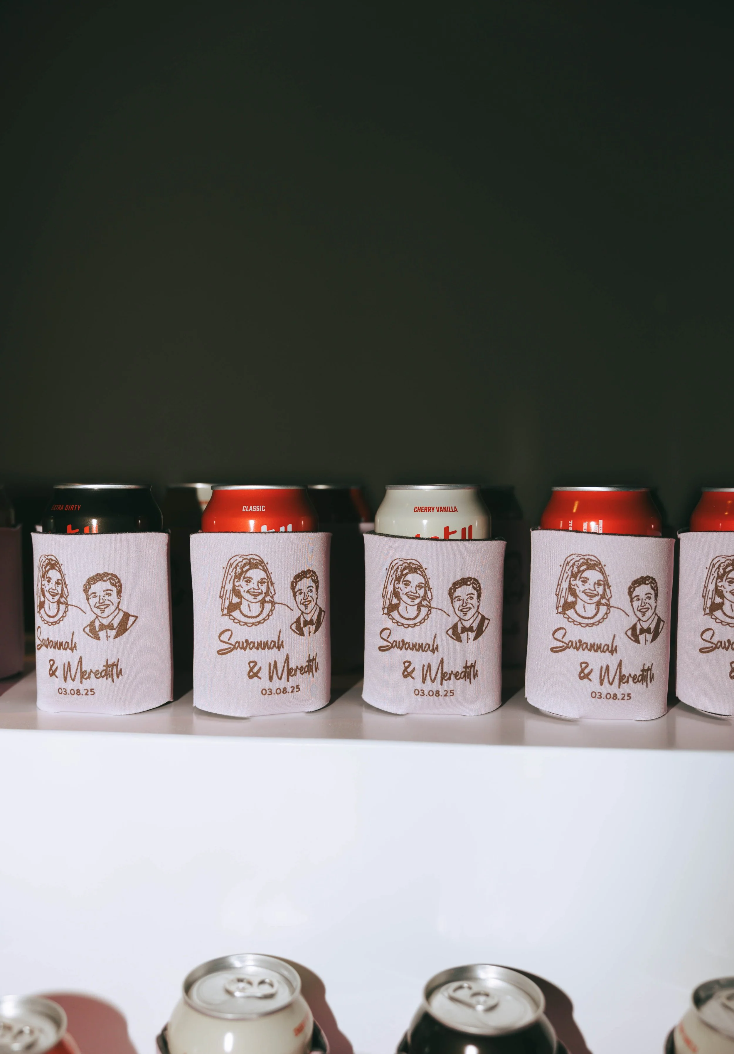 Pink can koozies printed with the couple's cartoon portraits and date, lined up with canned drinks