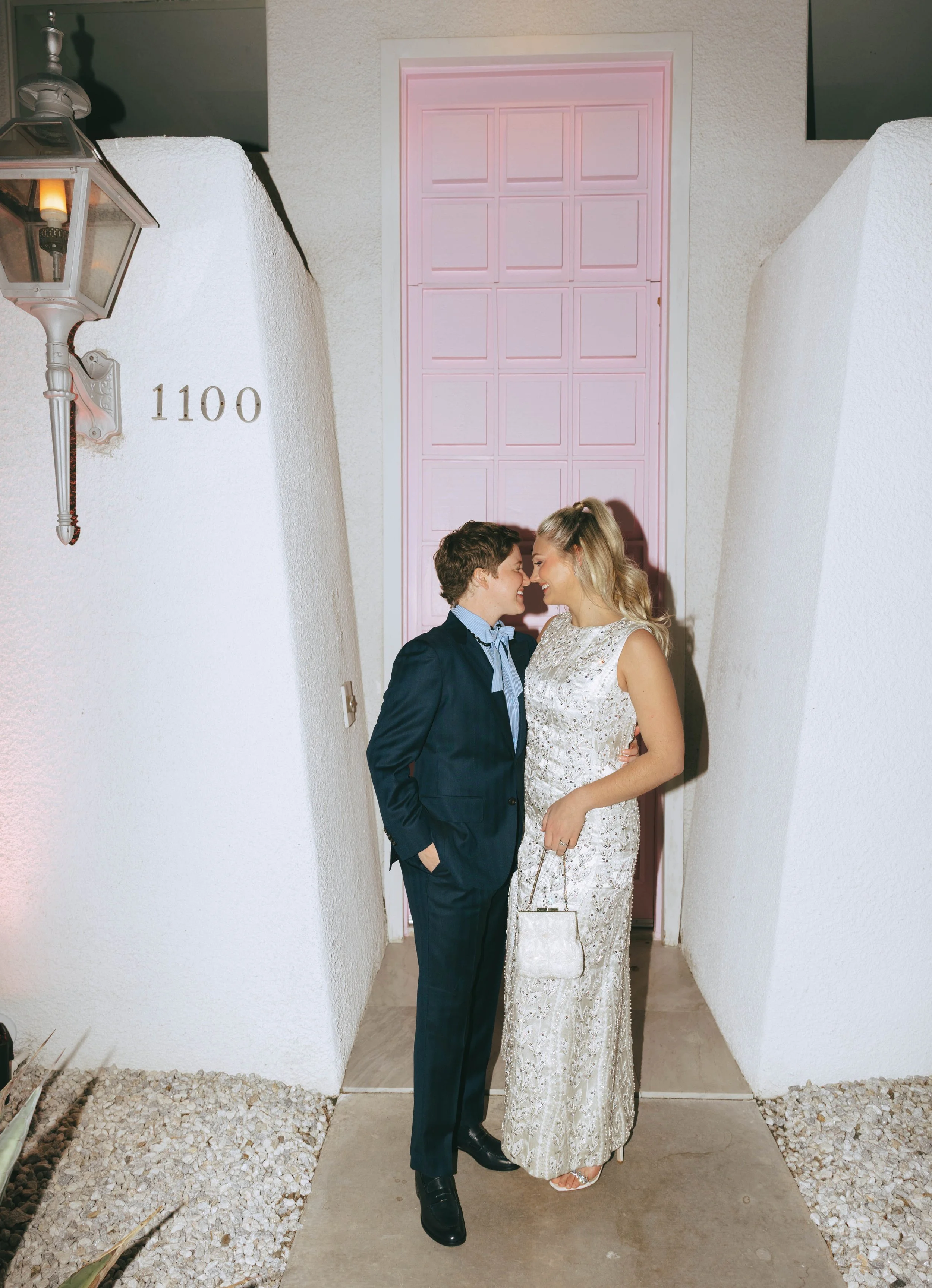 Bride and groom stand nose to nose in the narrow entry of the Pink Door House, its bright pink door behind them