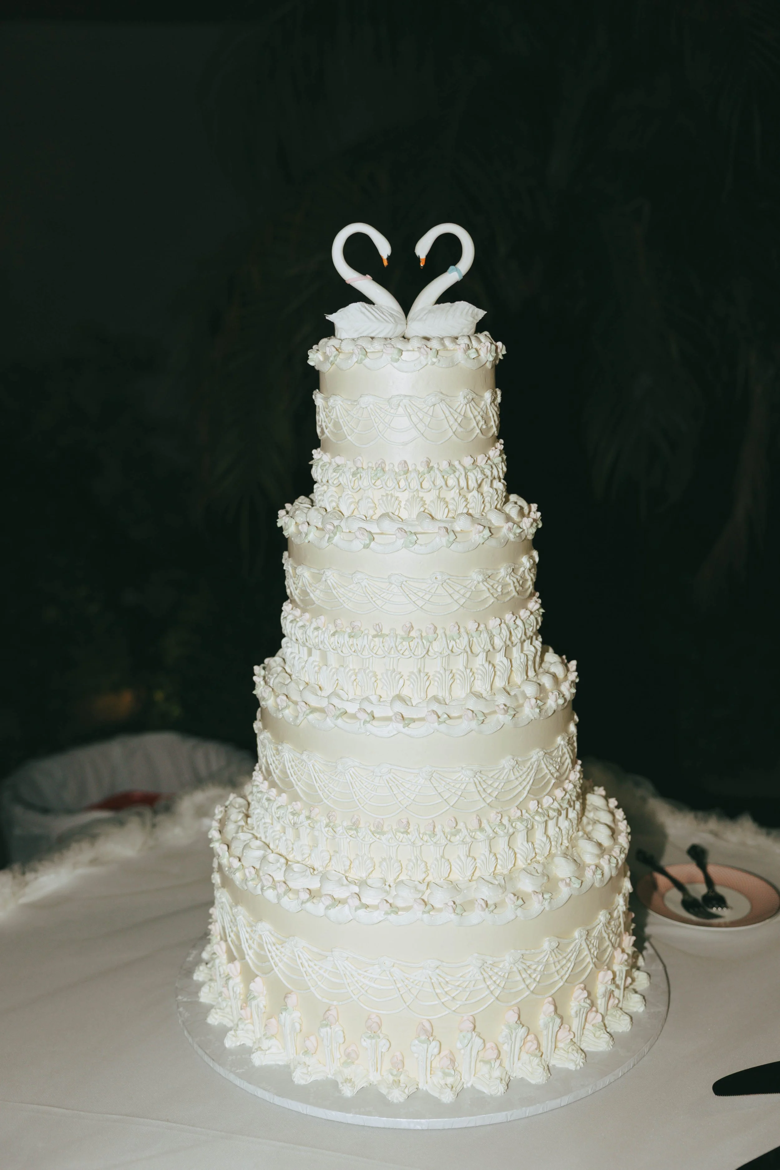 Wedding cake with tall white tiers of piped ruffles topped with two swans making a heart