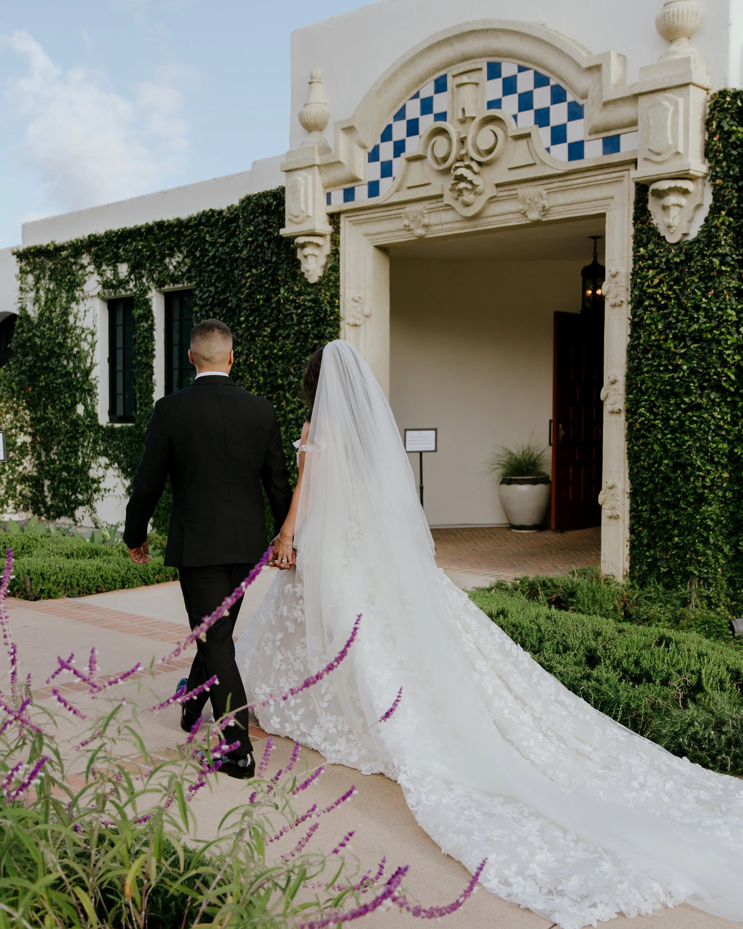 The newlyweds walk hand in hand toward the ivy-covered clubhouse entrance, the brides cathedral veil trailing behind