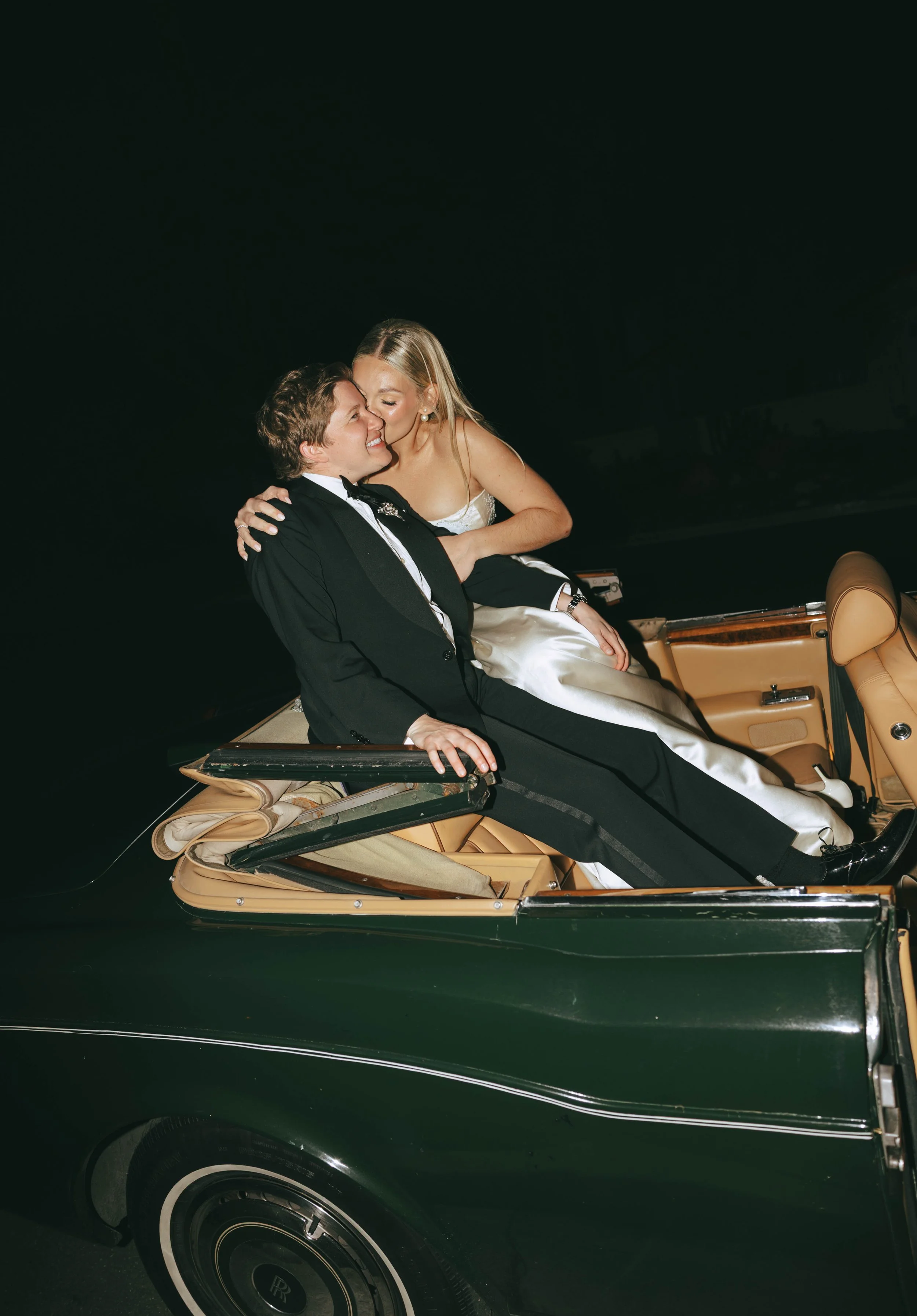 Bride and Groom sitting together on the back of a dark green vintage convertible at the end of the night