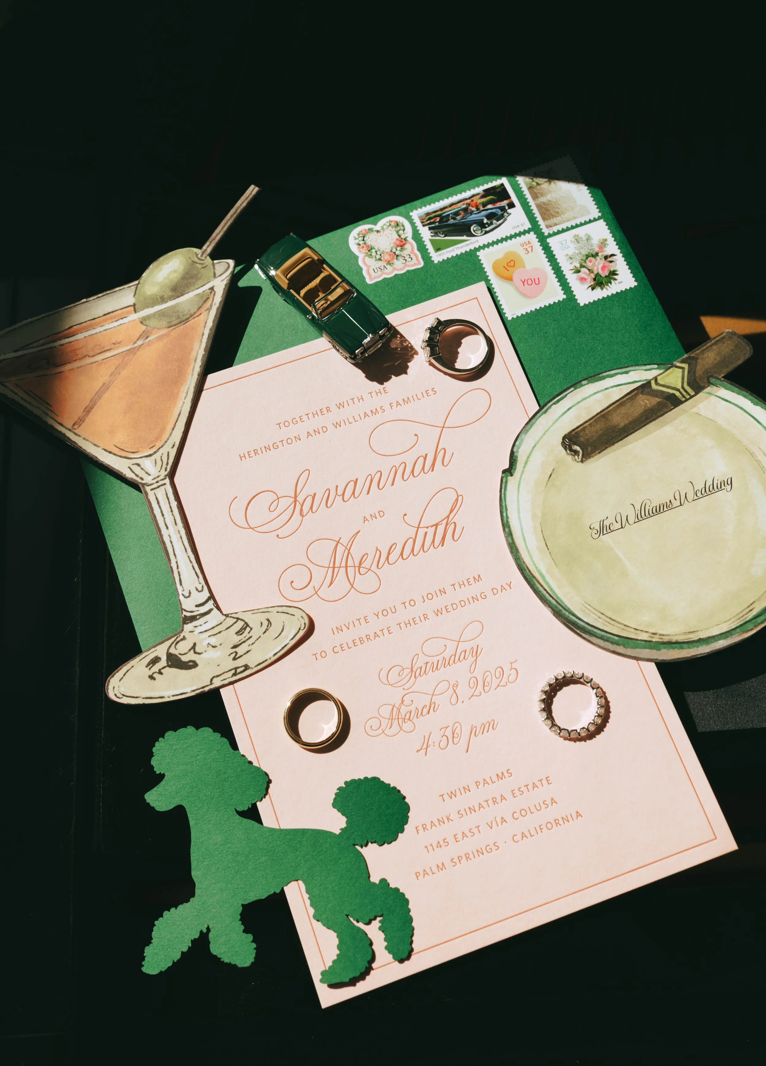 Pink letterpress invitation on dark green velvet with a die-cut green poodle, martini glass, cigar-tray card and wedding rings