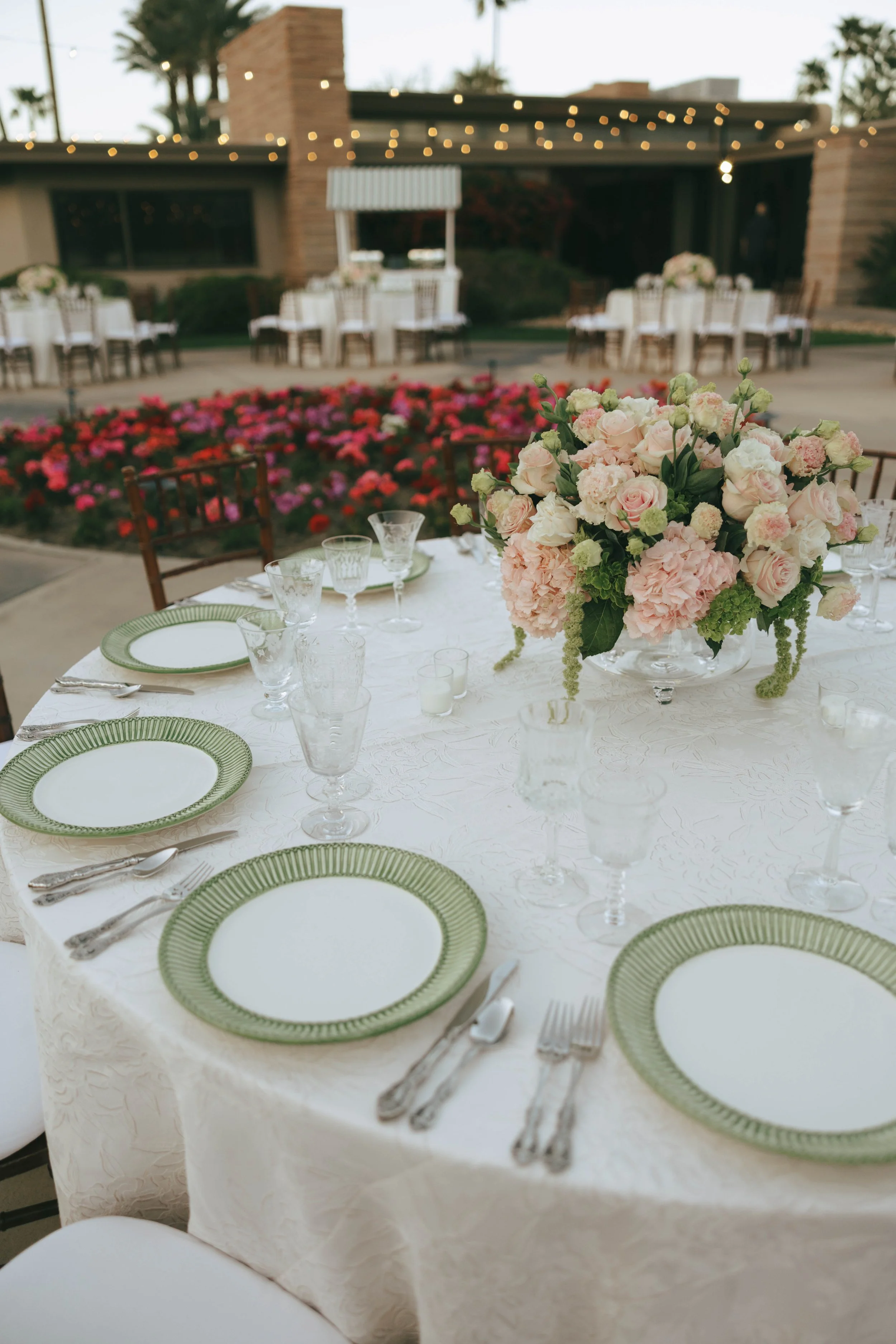 Place setting with green rimmed glass chargers, silver flatware and a blush garden rose centerpiece on ivory linen