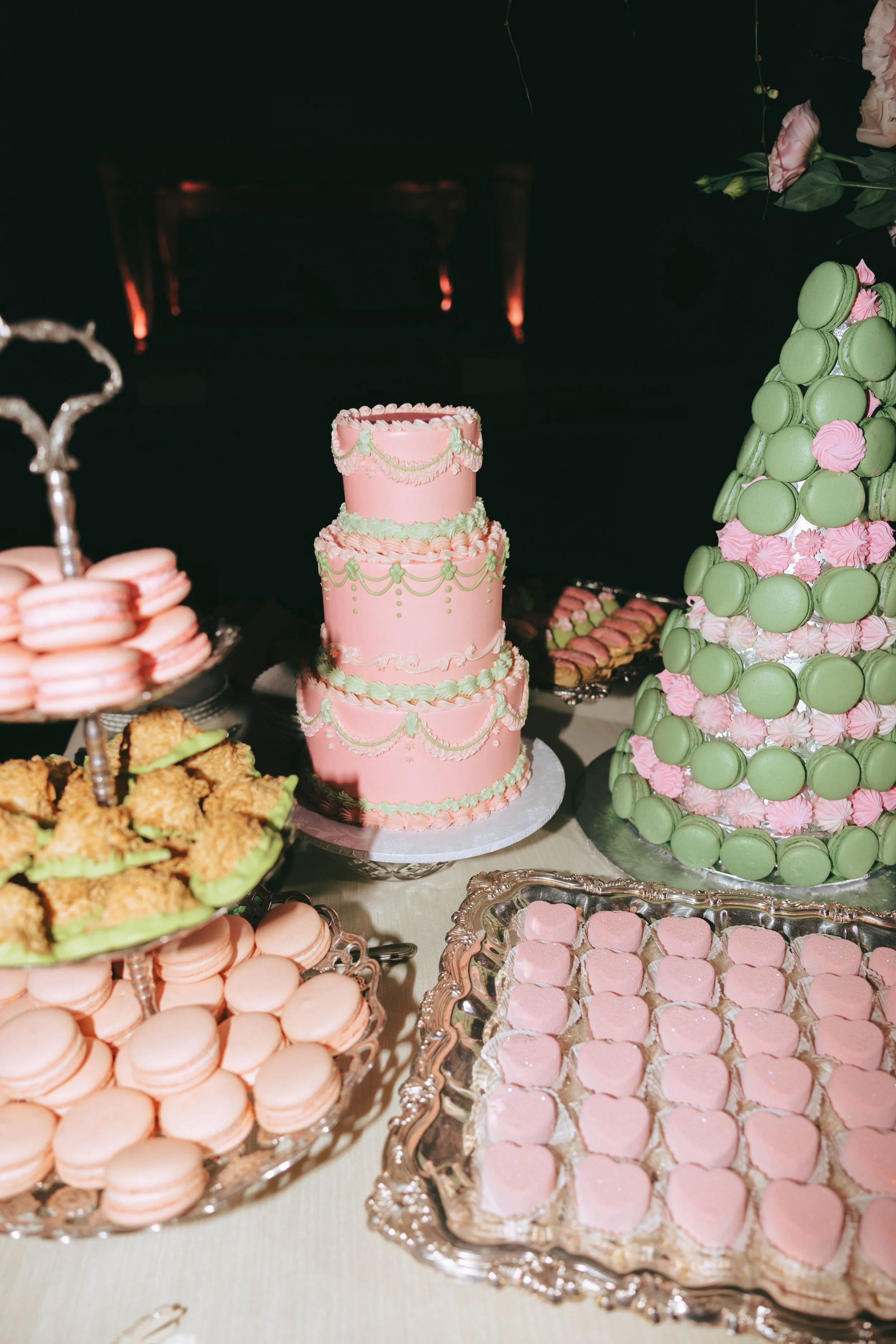 Dessert display with pink and green macaron towers, a pink tiered cake and trays of pastel petit fours