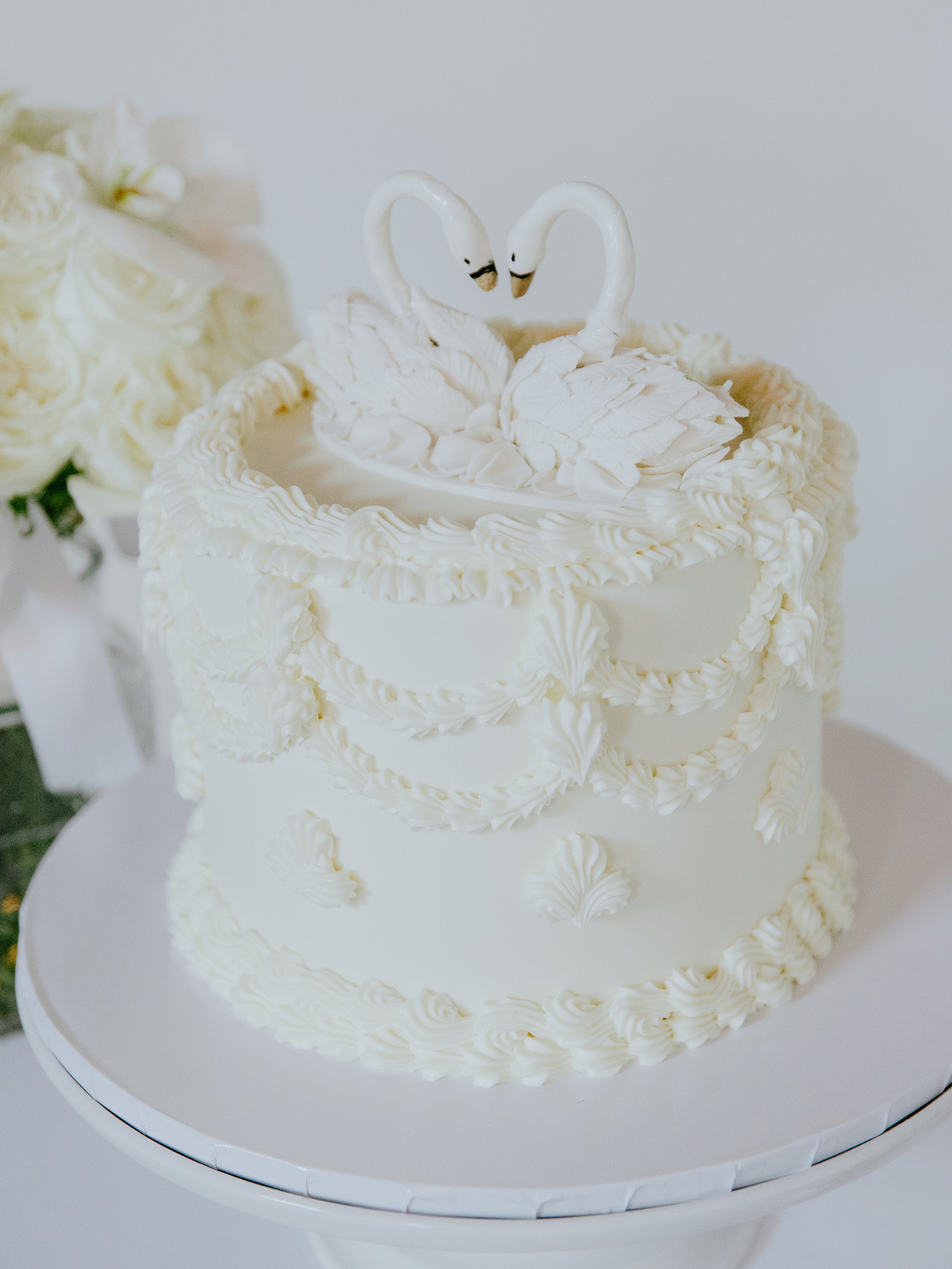 White buttercream wedding cake topped with a pair of swans