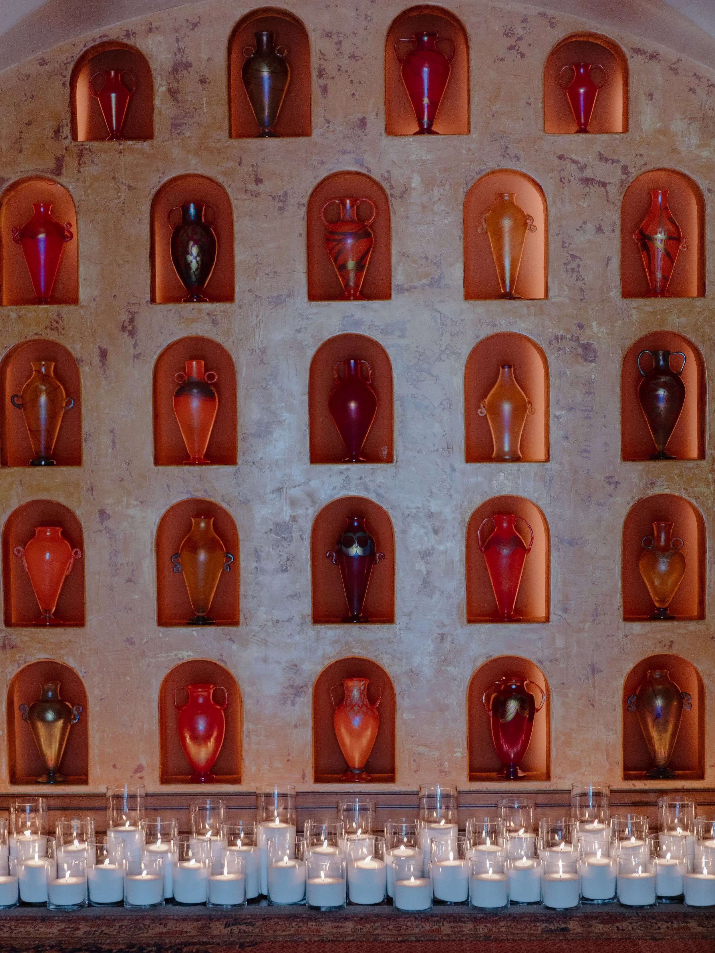 Wall of glowing glass vases set in arched niches, lined with pillar candles at the Montecito Club