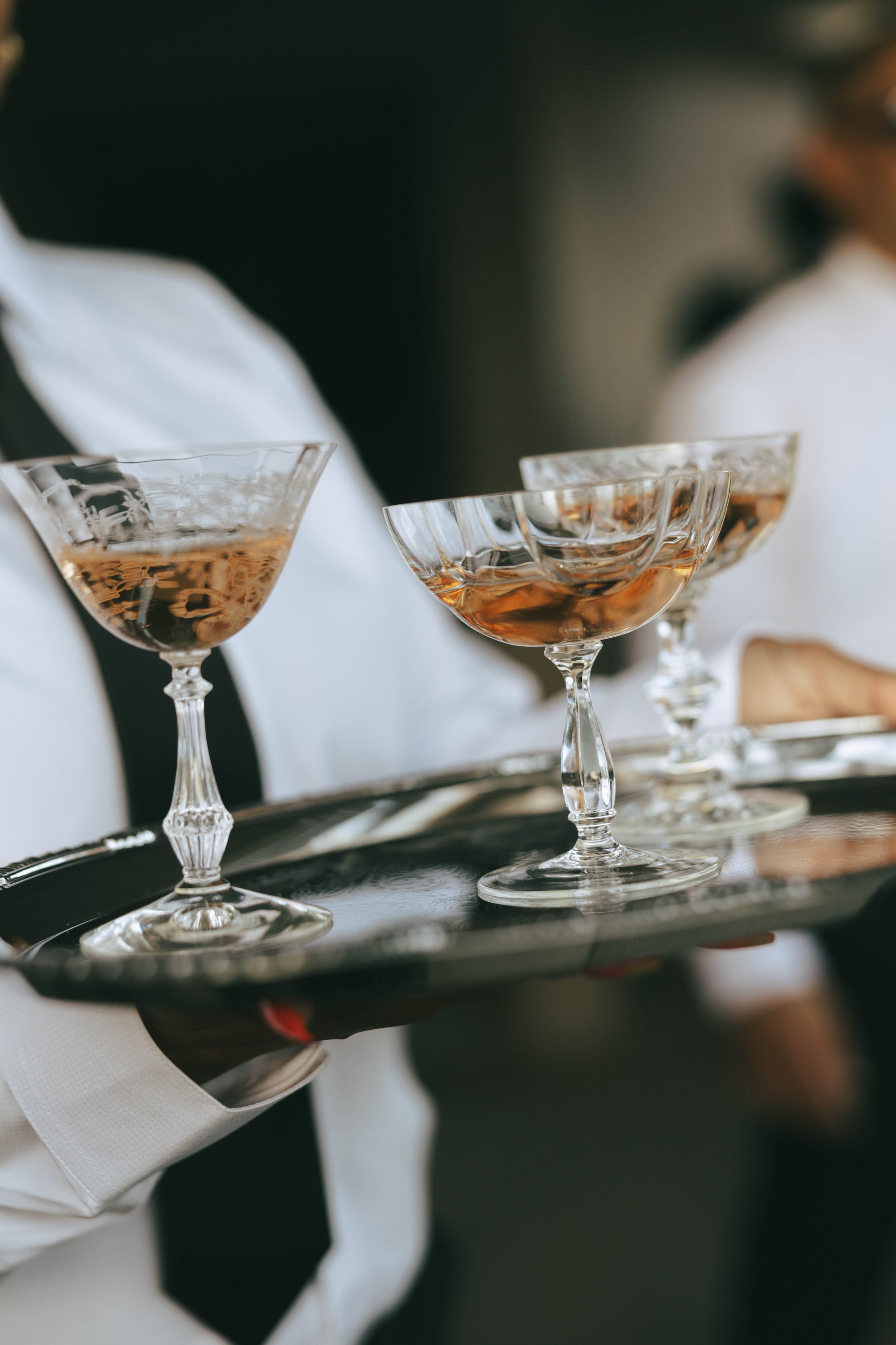 Server holding a silver tray of vintage etched champagne coupes filled with a blush cocktail