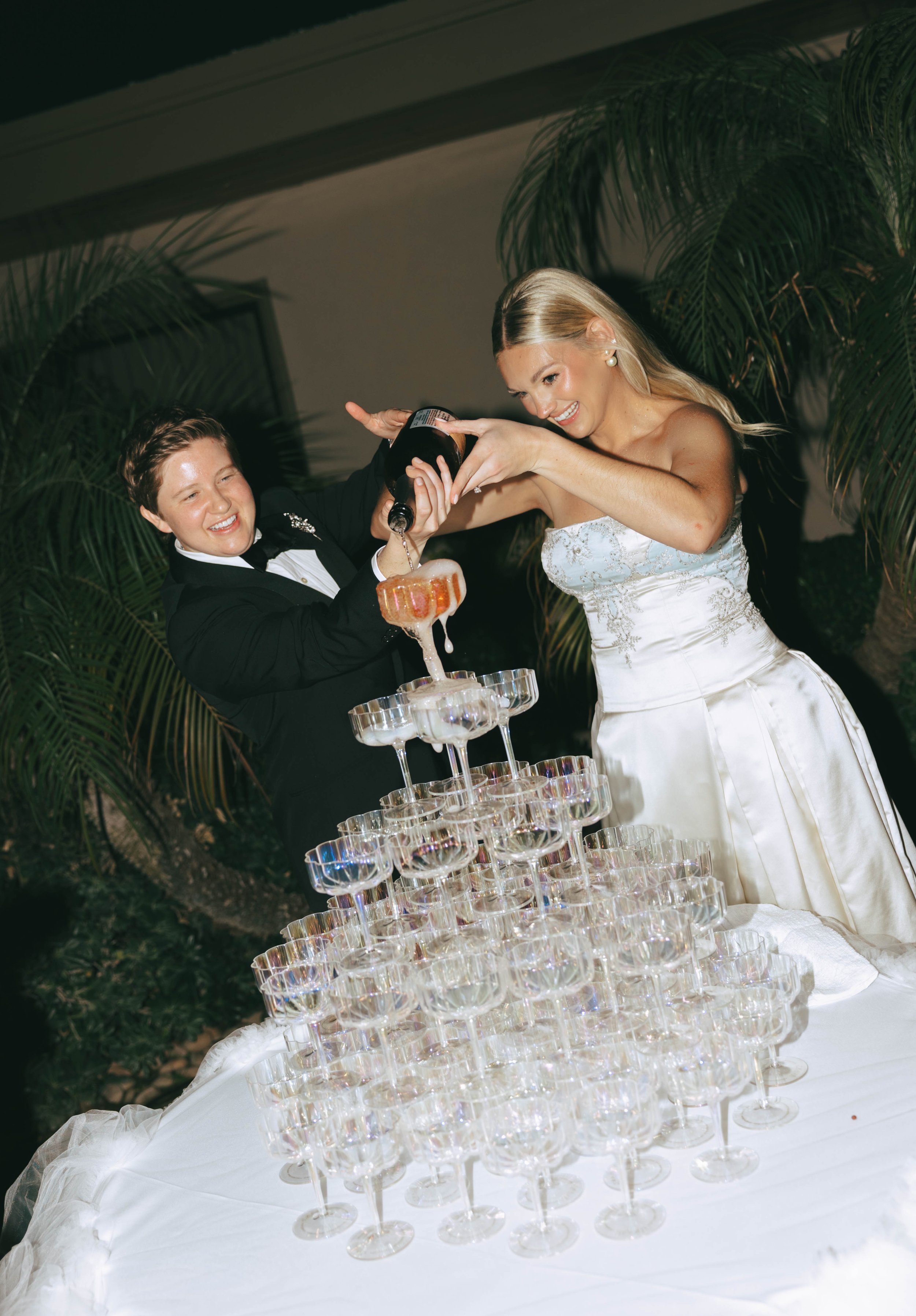 Bride and groom laughing as they pour champagne into the top coupe of the champagne tower.