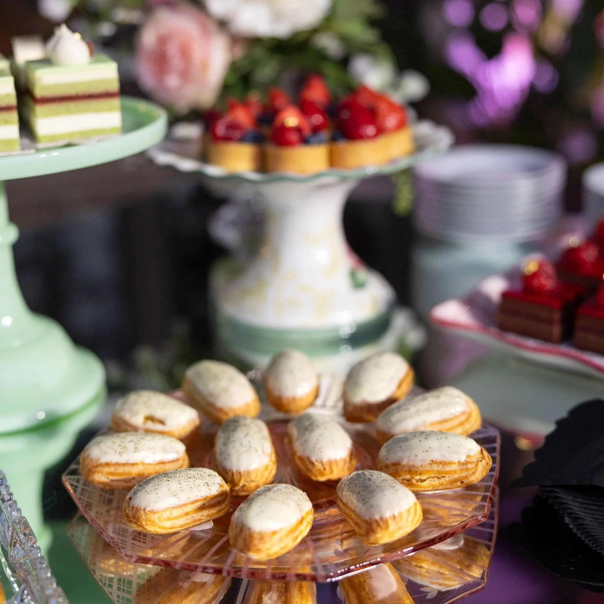Pastries table with eclairs. Strawberry cakes. Pastel color theme across the entire table. Floral arrangement alongside.