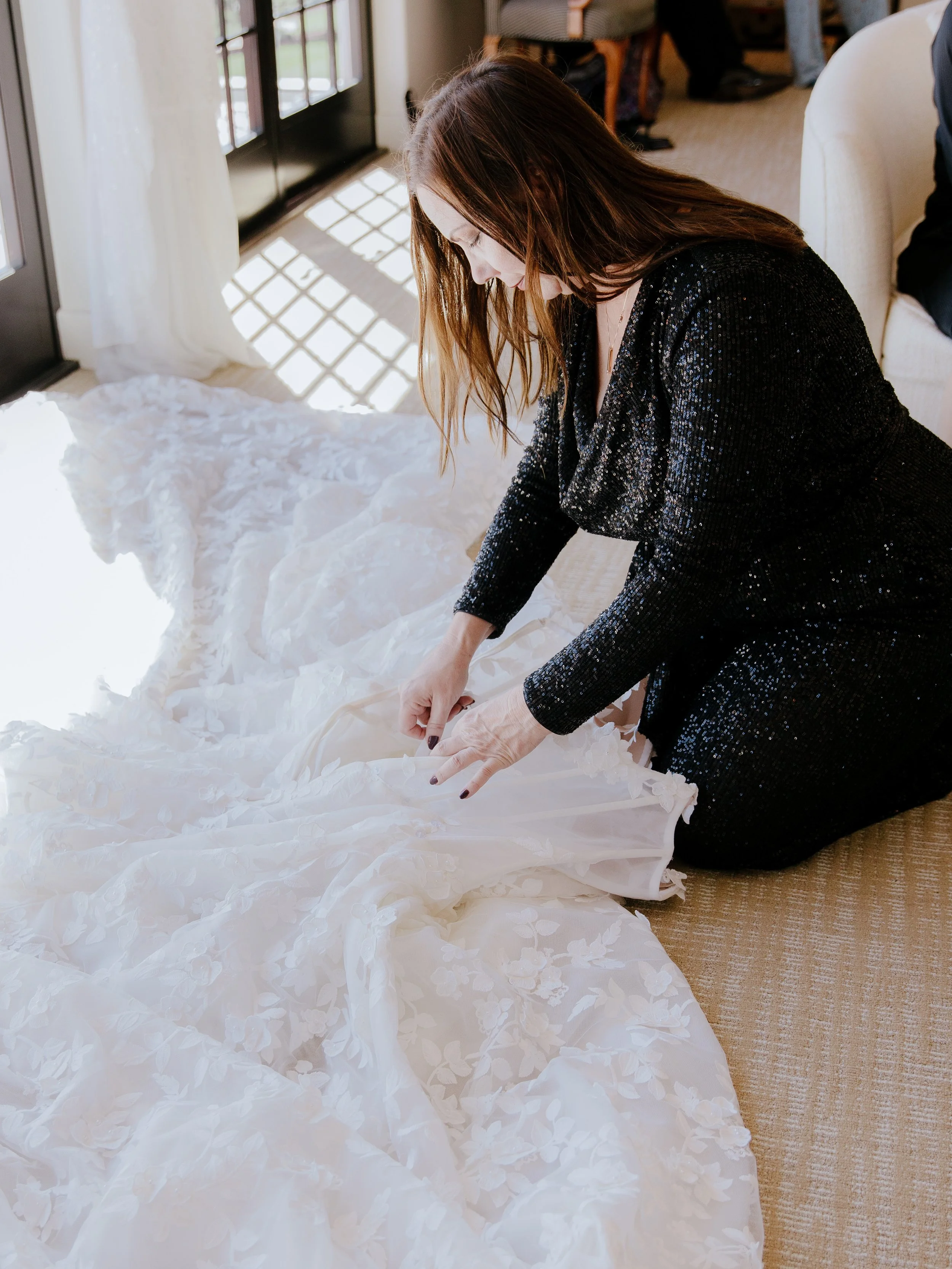 Event Planner Michele kneels to arrange the train of Blanca's Galia Lahav gown