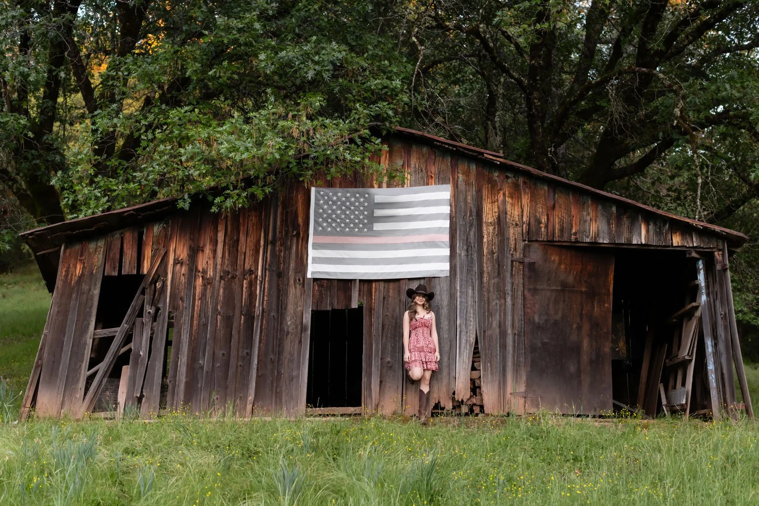 eighth grade girl leans against old barn which has an American flag on it