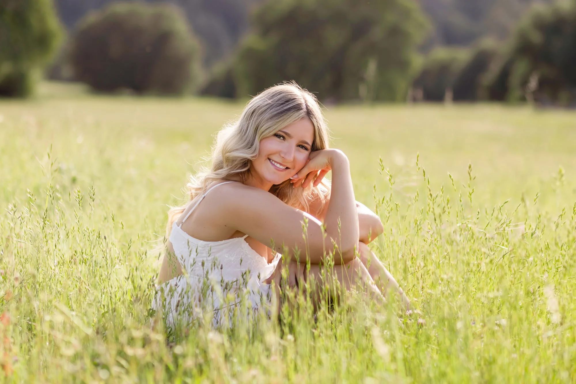 High school senior girl wearing a white dress sits in a grassy field in Pilot Hill, California