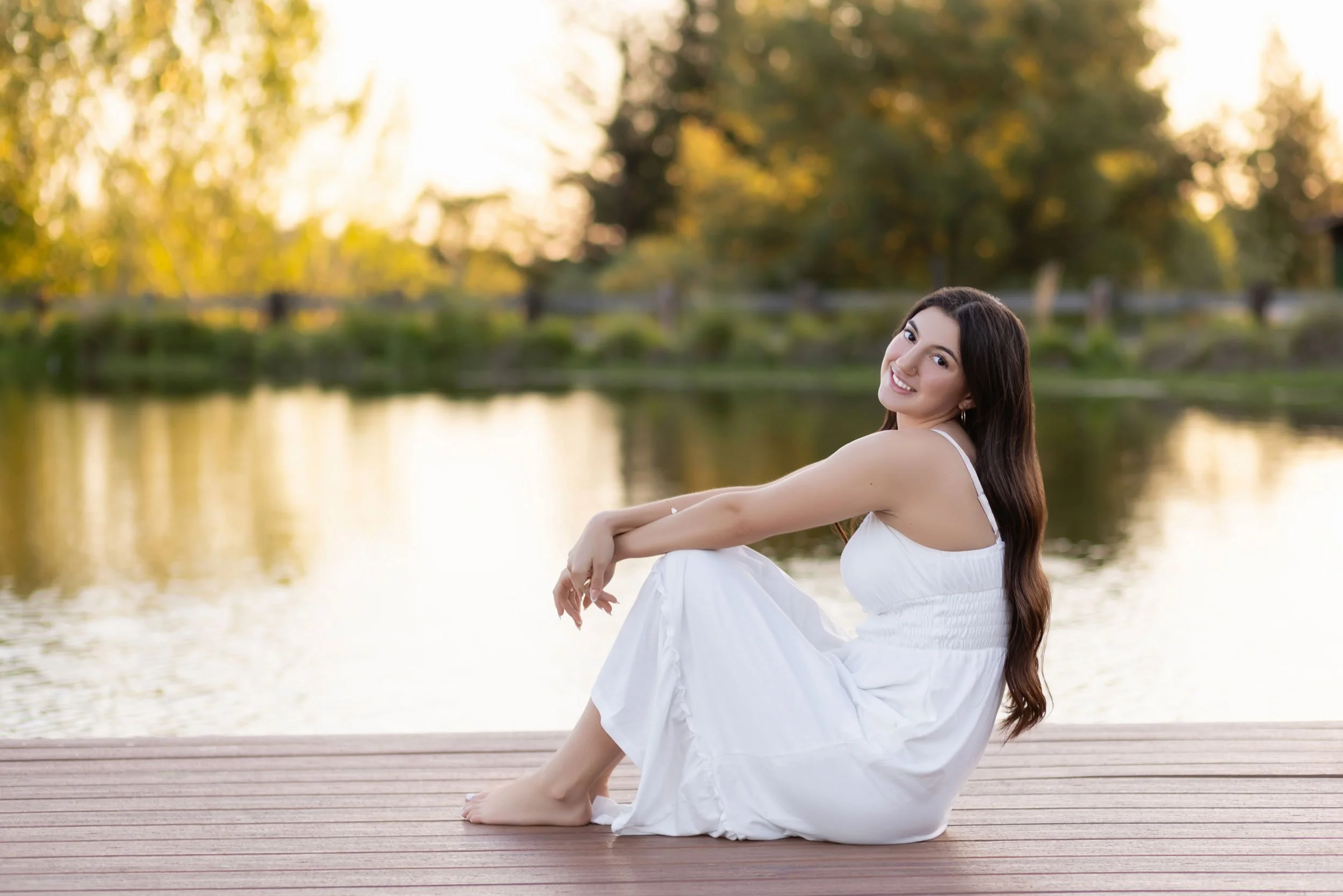 Colfax High School Senior Maddie wears a long white dress while sitting on the wood dock at Bywater Hollow Lavender Farm in Lincoln, California in the spring of 2026