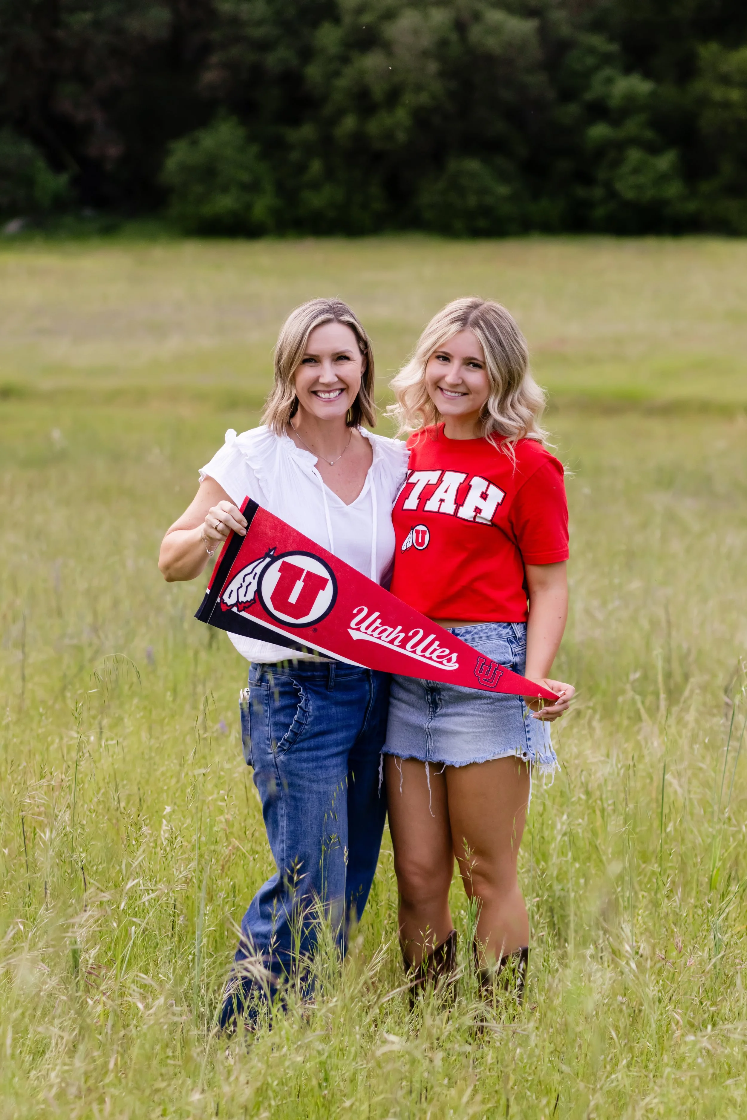 Whitney high school senior wearing red Utah ute shirt poses in grassy field with mom holding Utah Utes pennant