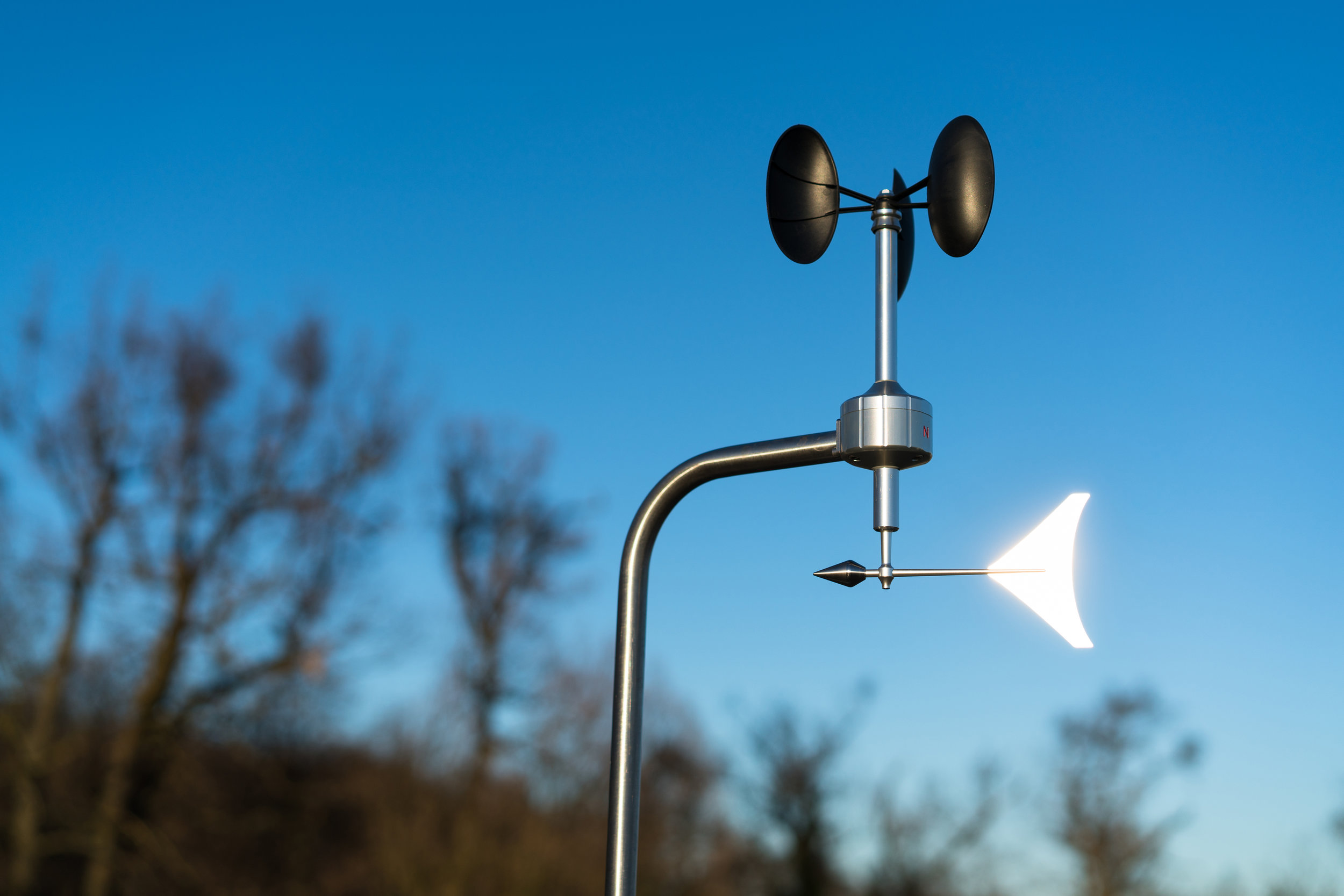 Anemometer with wind vane with blue sky and brown trees