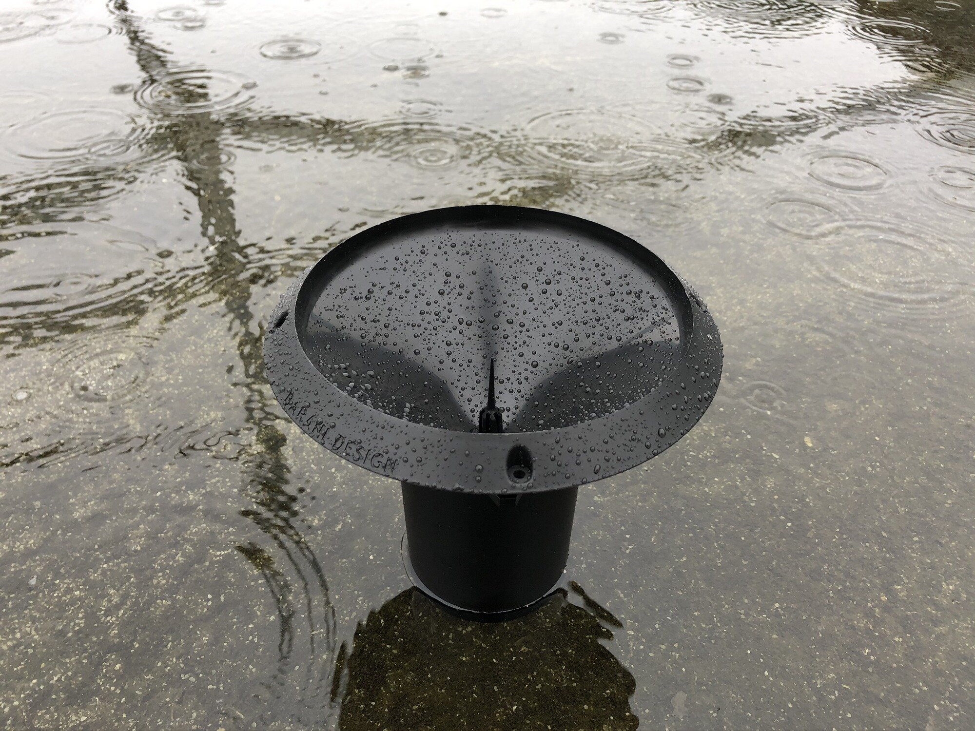  MeteoRain IoT Compact wireless automatic rain gauge right after a thunderstorm surrounded by rainwater showing raindrop impacts. 