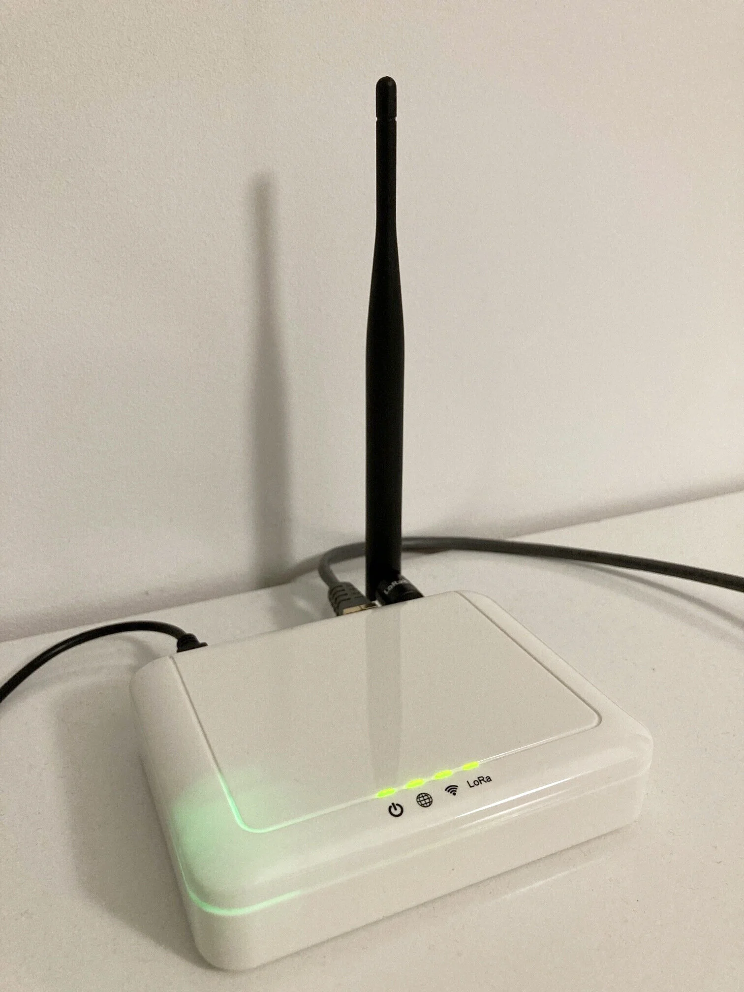 Gemtek Browan WLRGFM-100 Indoor Femto LoRaWAN gateway with an upright external antenna, connected cables, and all four front indicator lights solid green.