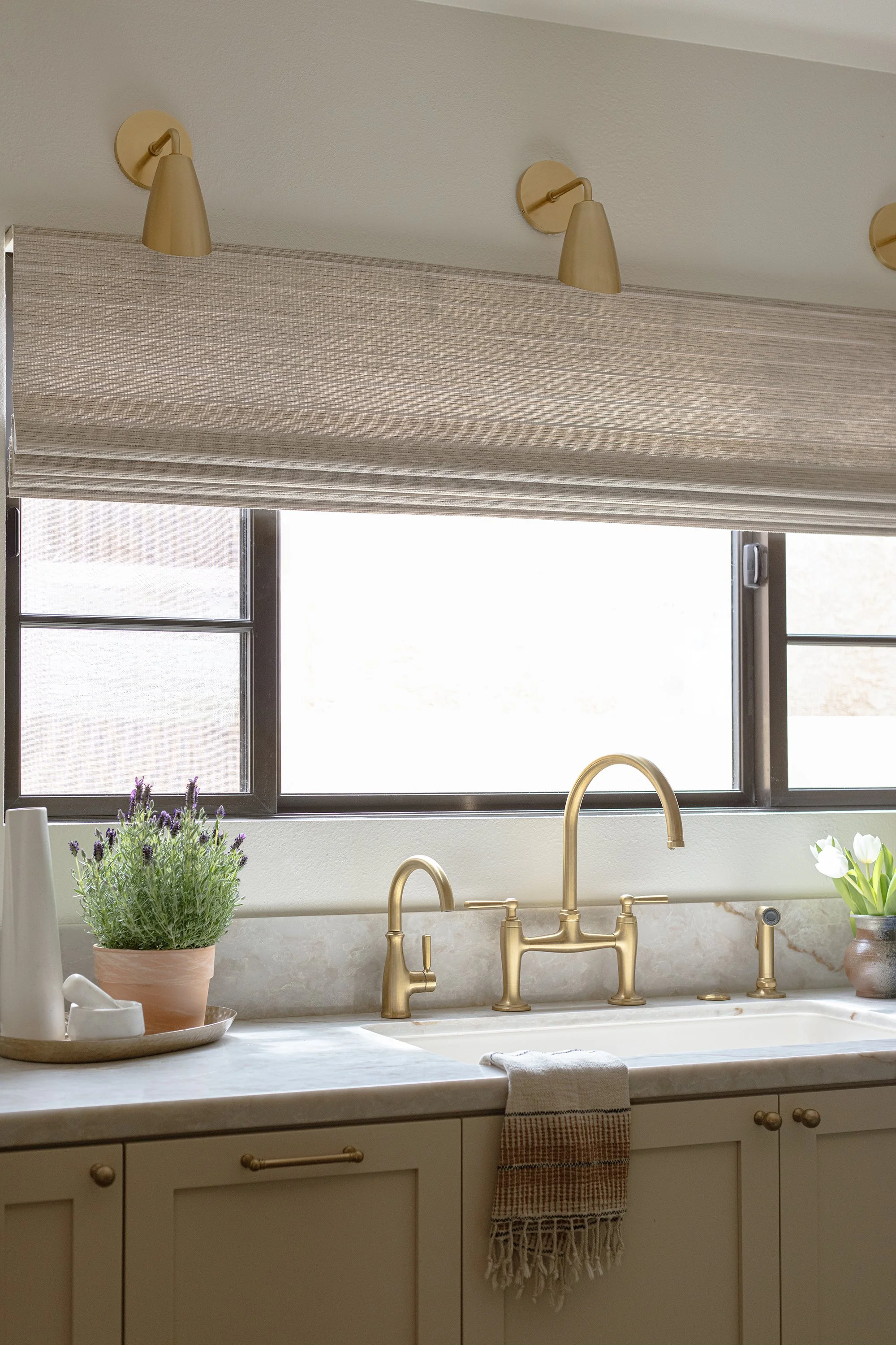 kohler aged brass faucet, brass hardware, gallery rail, cream cabinets, vintage lighting, taj mahal stone, aged brass light fixtures, aged brass, vintage kitchen, kitchen renovation, white oak wainscot, ivory cabinets, linen roman shades