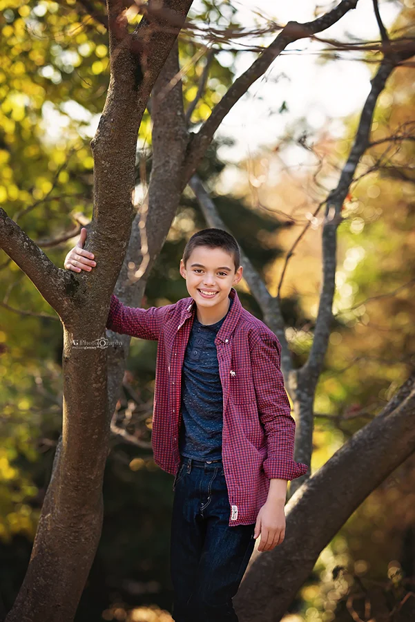 Boy smiling while climbing tree during a family photoshoot with the best photographer in Bergen County