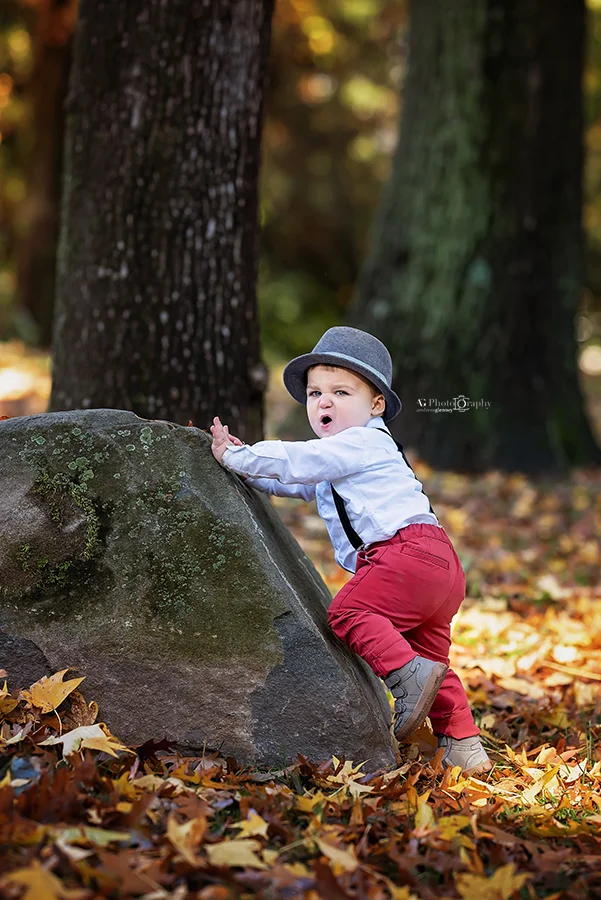 Little boy climbing a rock during a fun photoshoot outdoor in Bergen County