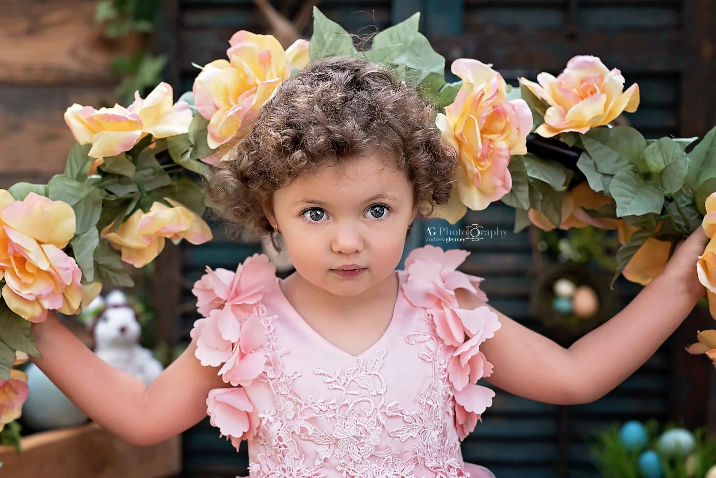 Little girl with curly hair holding flower prop and wearing a pink dress photographed for a Spring session in Bergen County