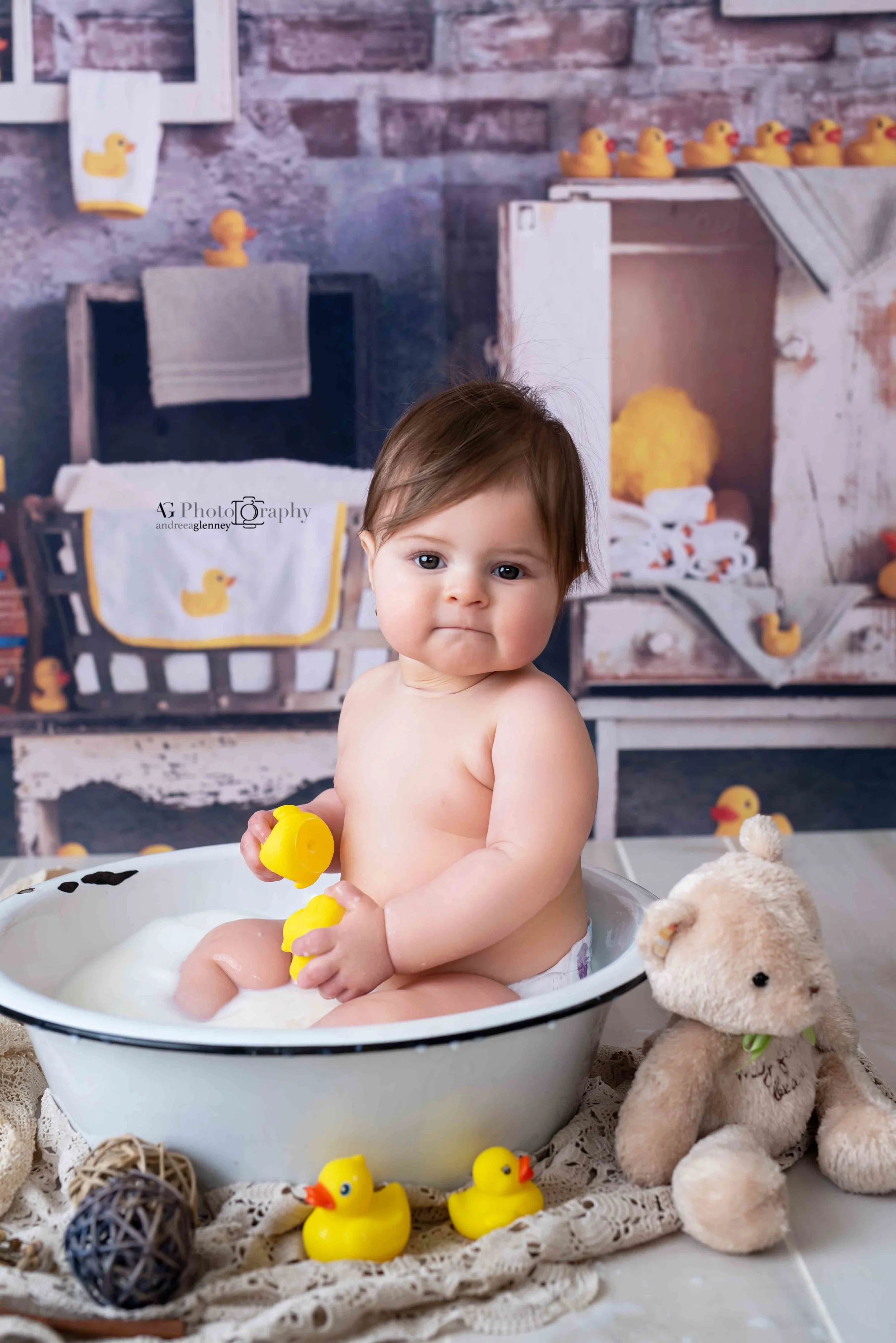 Baby girl playing with rubber duckie in a bath tub during a bath photoshoot in Bergen County