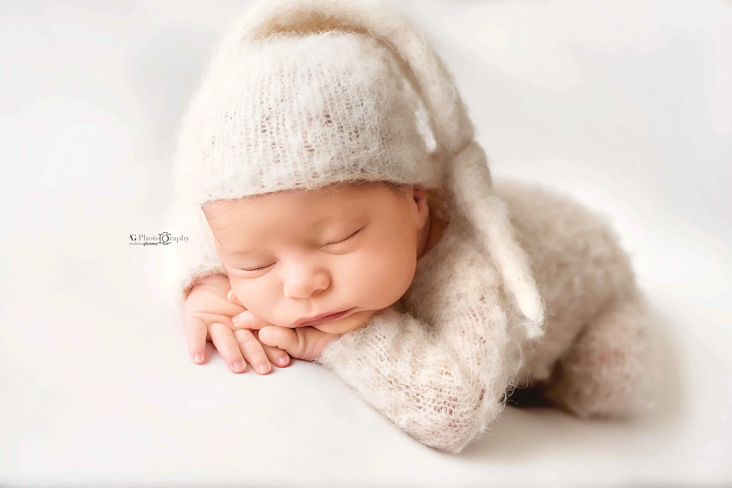 Newborn baby wearing neutral color outfit posed sleeping with chin on his hands during a Newborn photoshoot with a Bergen County Photographer