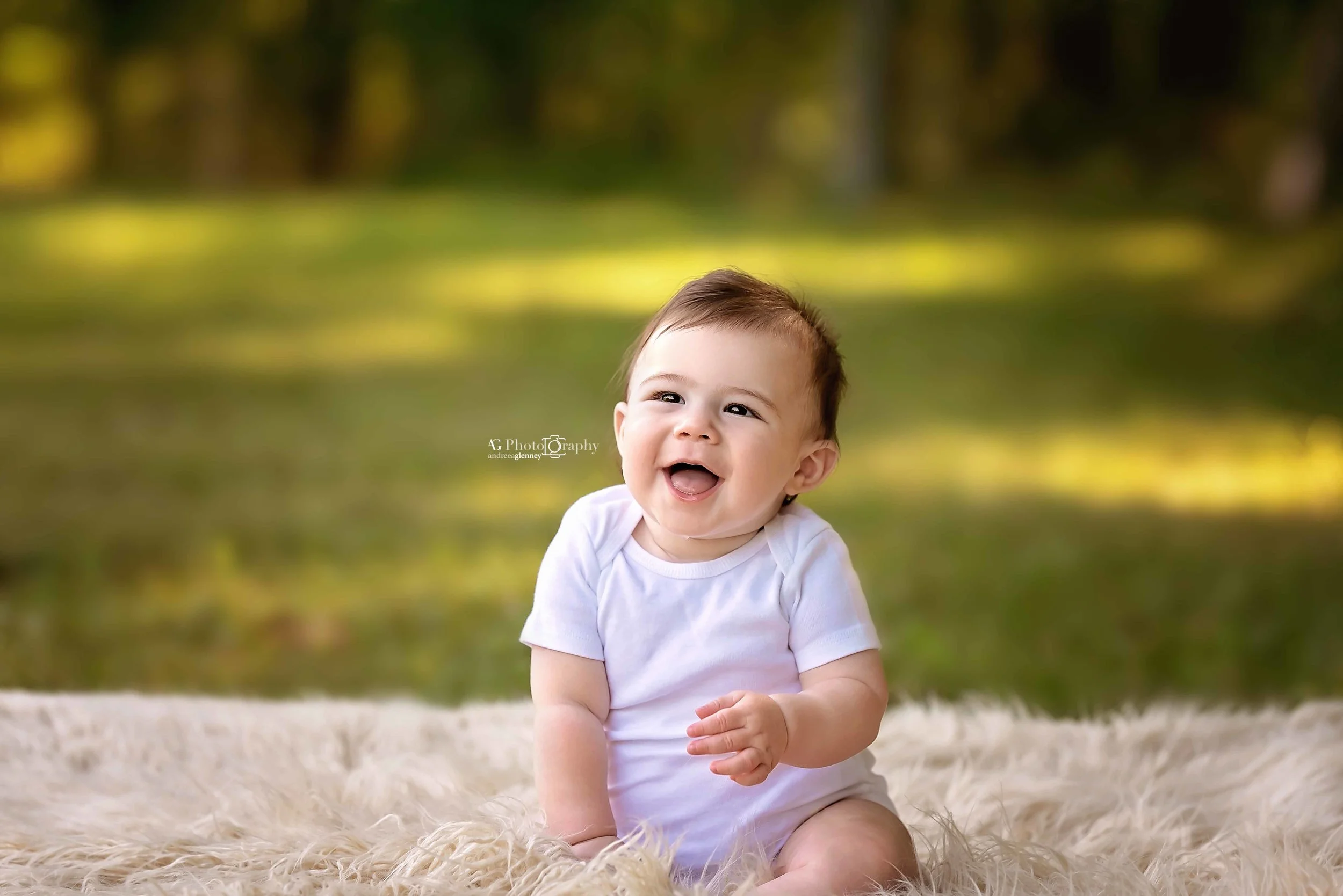 Baby boy sitting on a tan blanket outdoor laughing while being photographed in Bergen County, New Jersey