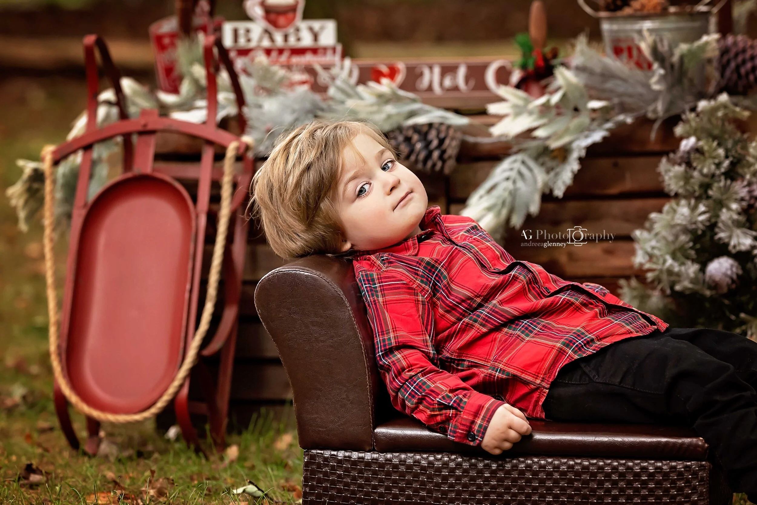 Little boy wearing Holiday shirt laying down on a small couch during a hot coca mini session in Bergen County, NJ