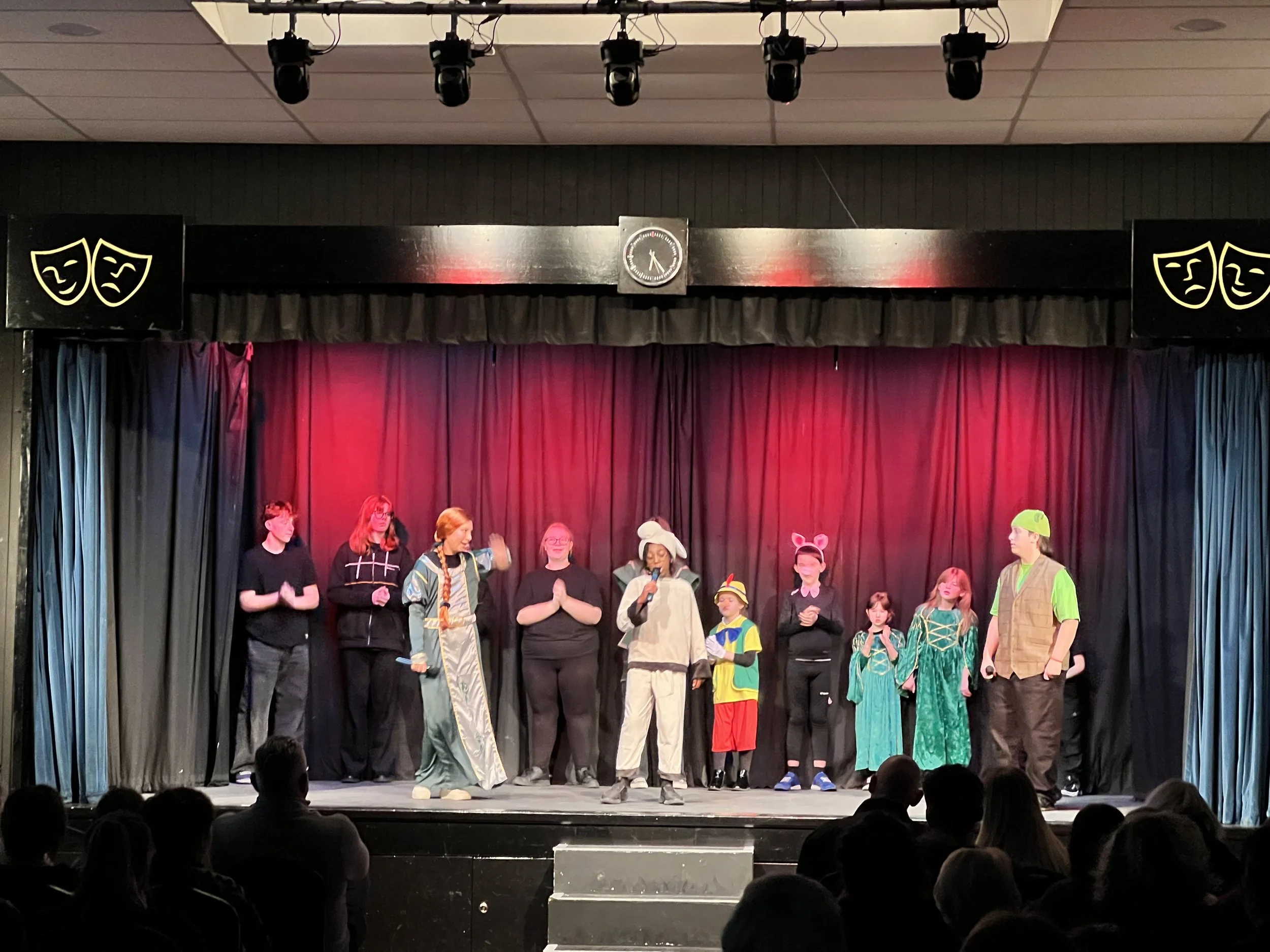 Children performing on a stage dressed in costumes, with an audience watching.